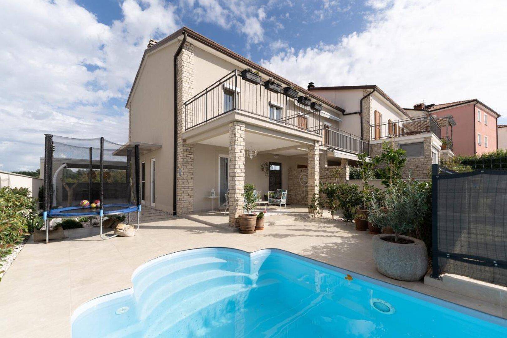 Gesamtansicht des modernen Hauses mit Pool, Trampolin und überdachter Terrasse.