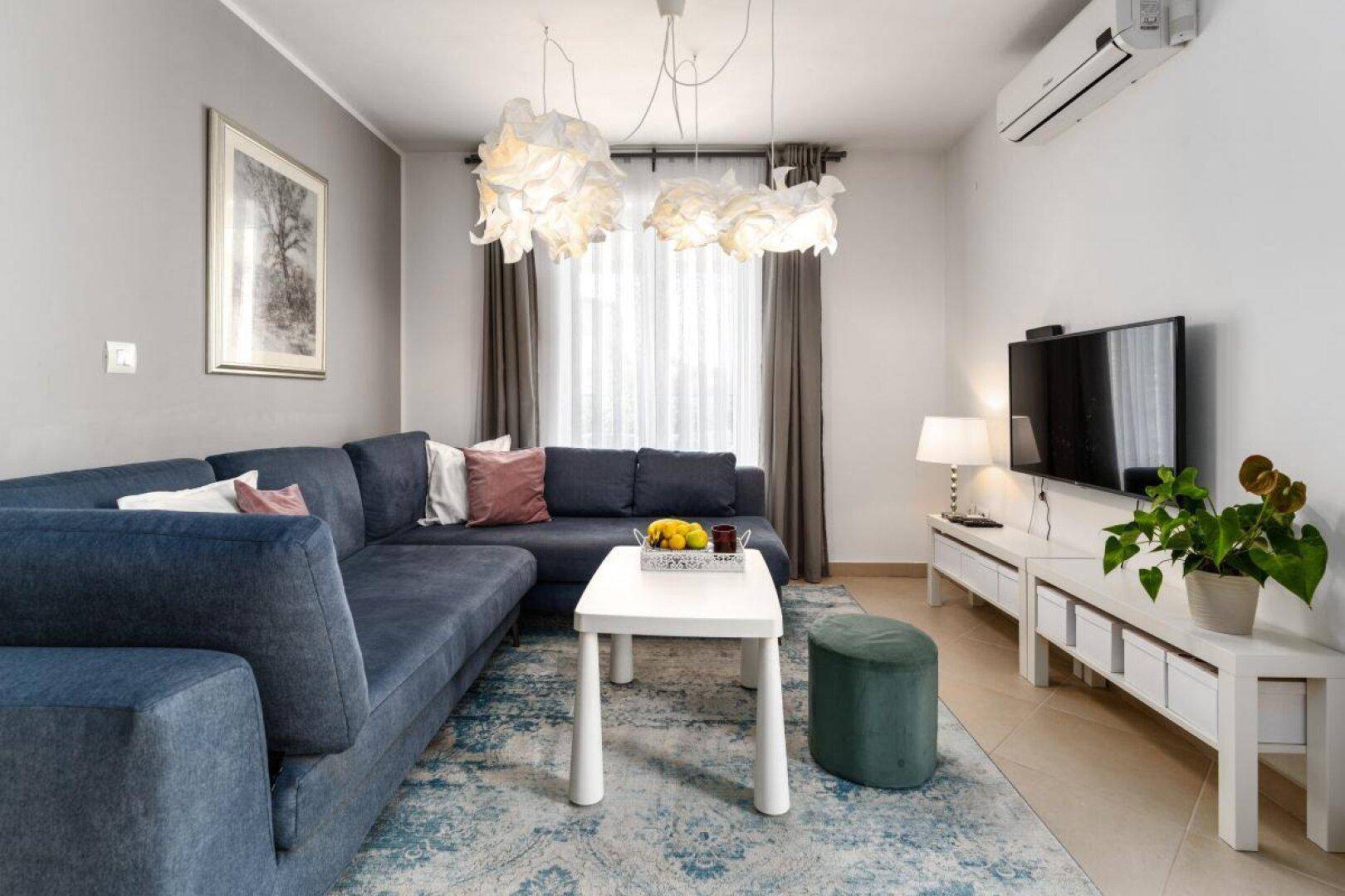 Helles Wohnzimmer mit blauem Ecksofa, modernem Couchtisch und dekorativen Hängelampen.