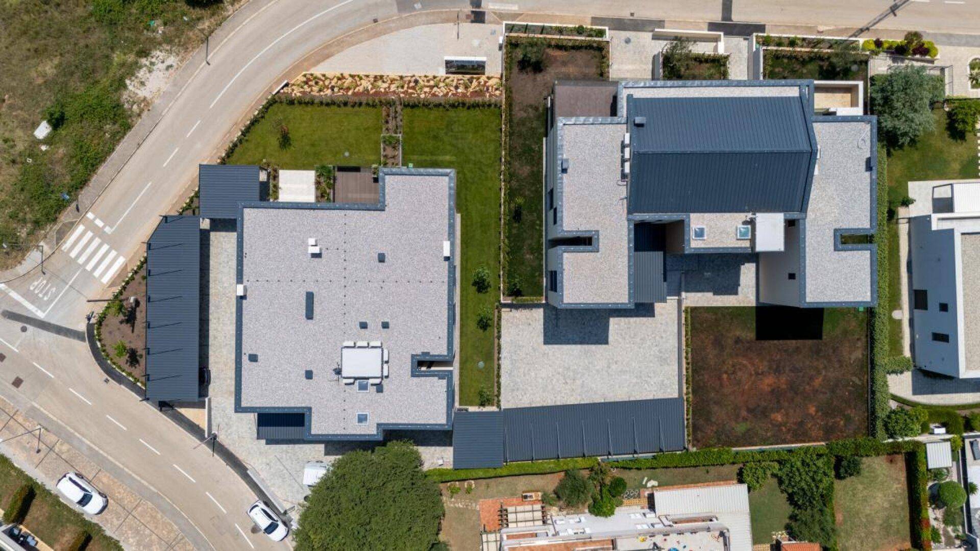 Vogelperspektive auf zwei moderne Gebäude mit Flachdächern und angrenzenden Grundstücksflächen sowie Parkplätzen.