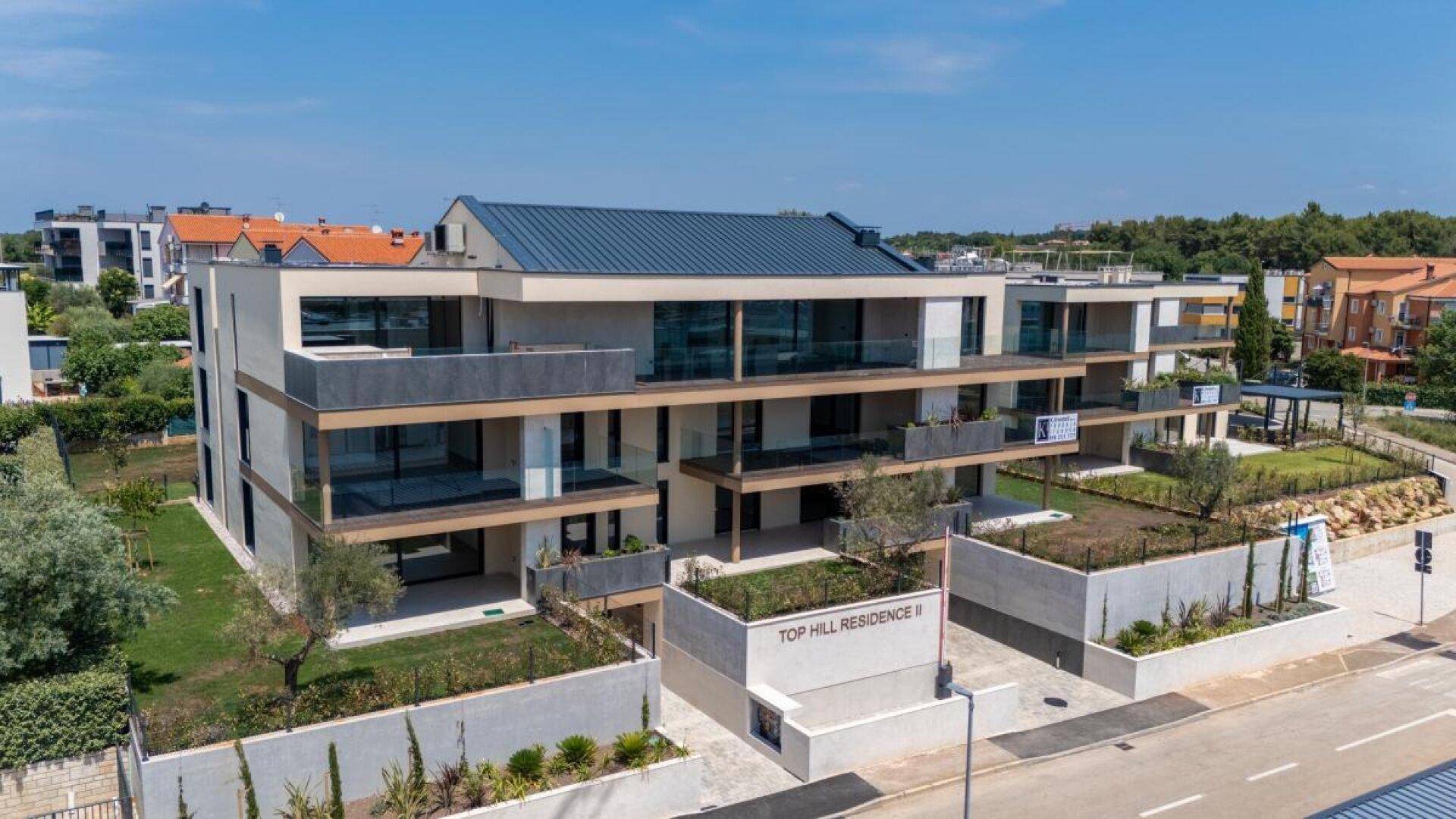 Ansicht eines modernen Wohnkomplexes mit Flachdach, Balkonen und gepflegten Grünflächen unter strahlendem Himmel.