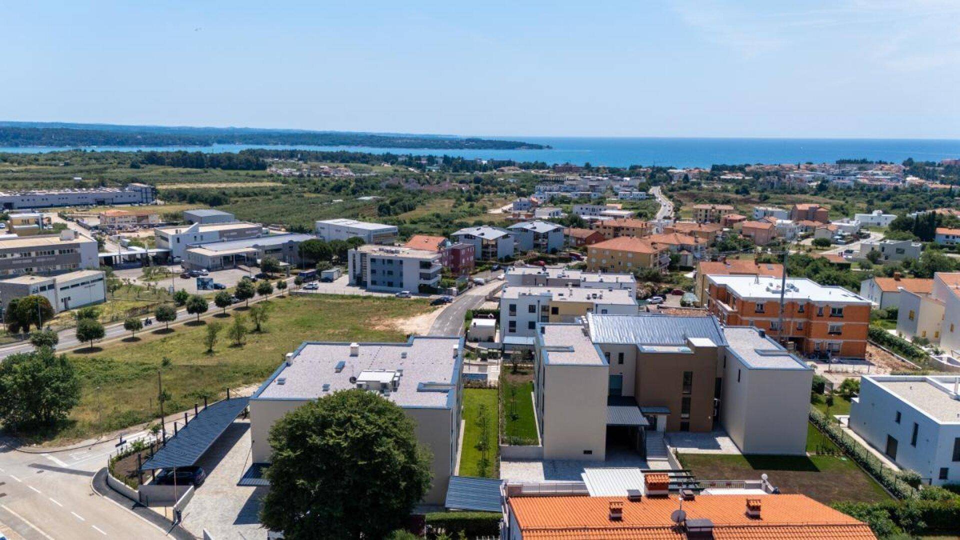 Weitläufige Luftaufnahme der Küstenregion mit Wohngebäuden, viel Grün und dem Meer in der Ferne.