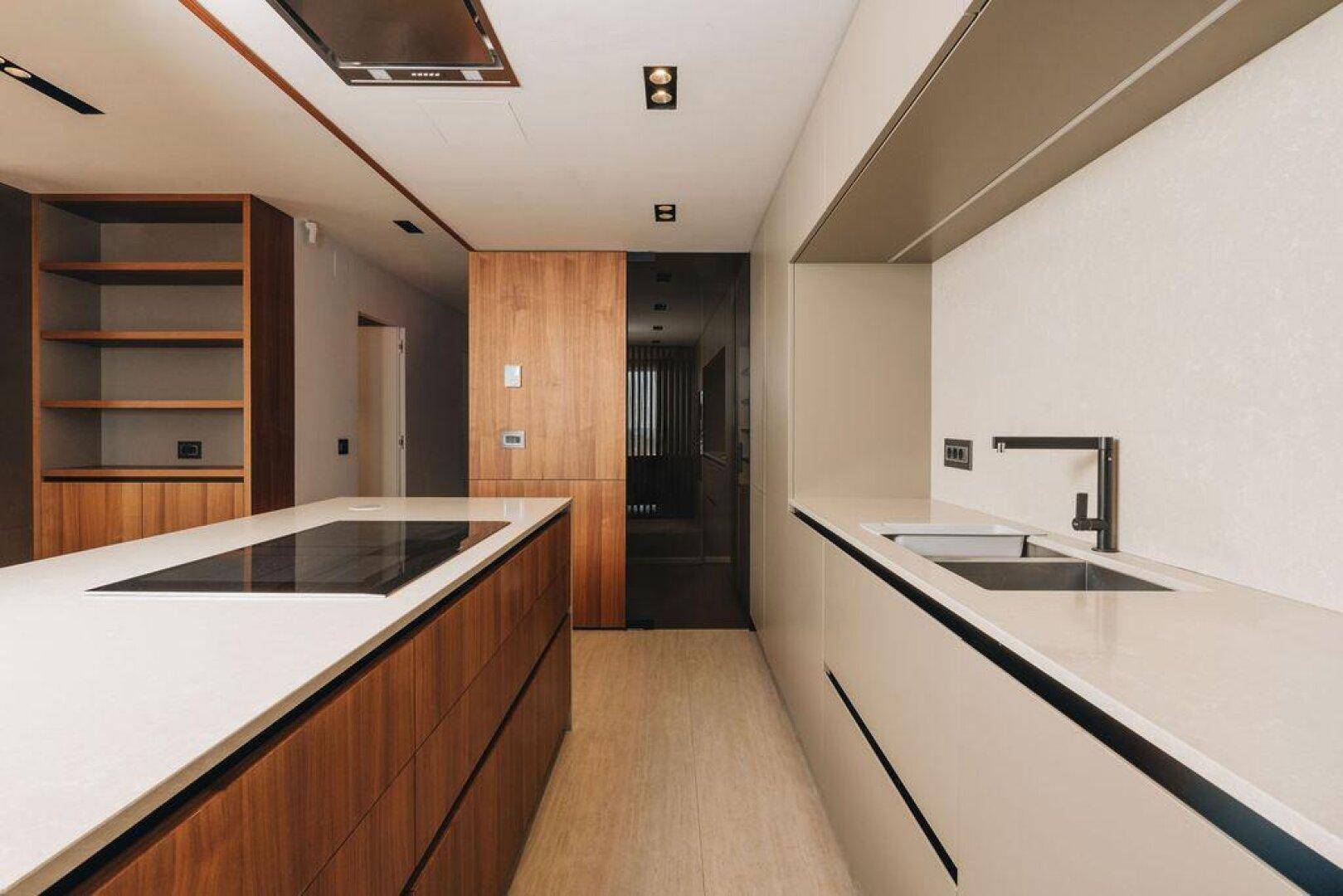 Detailansicht der modernen Küche mit Spüle, Kochinsel und eleganten Holzschubladen.