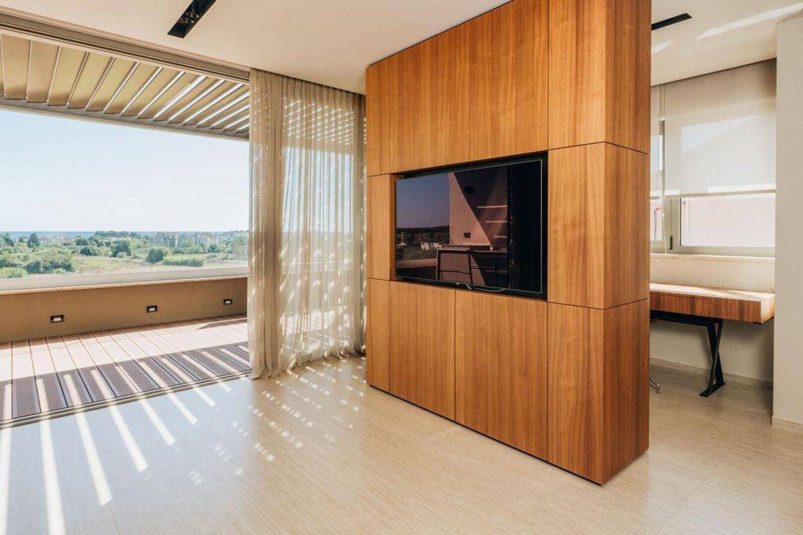 Wohnbereich mit Holzwand und integriertem Fernseher, Zugang zu einer sonnigen Terrasse.