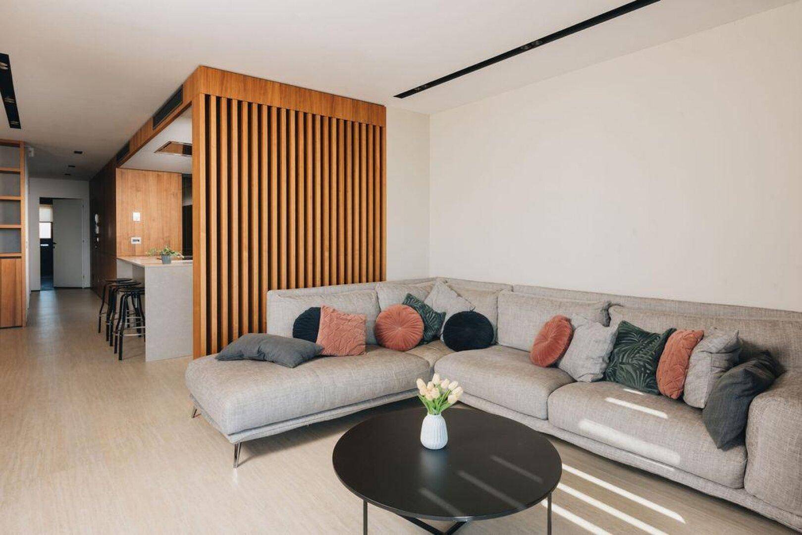 Modernes Wohnzimmer mit Ecksofa, Couchtisch und Holzelementen, offen zum Küchenbereich.