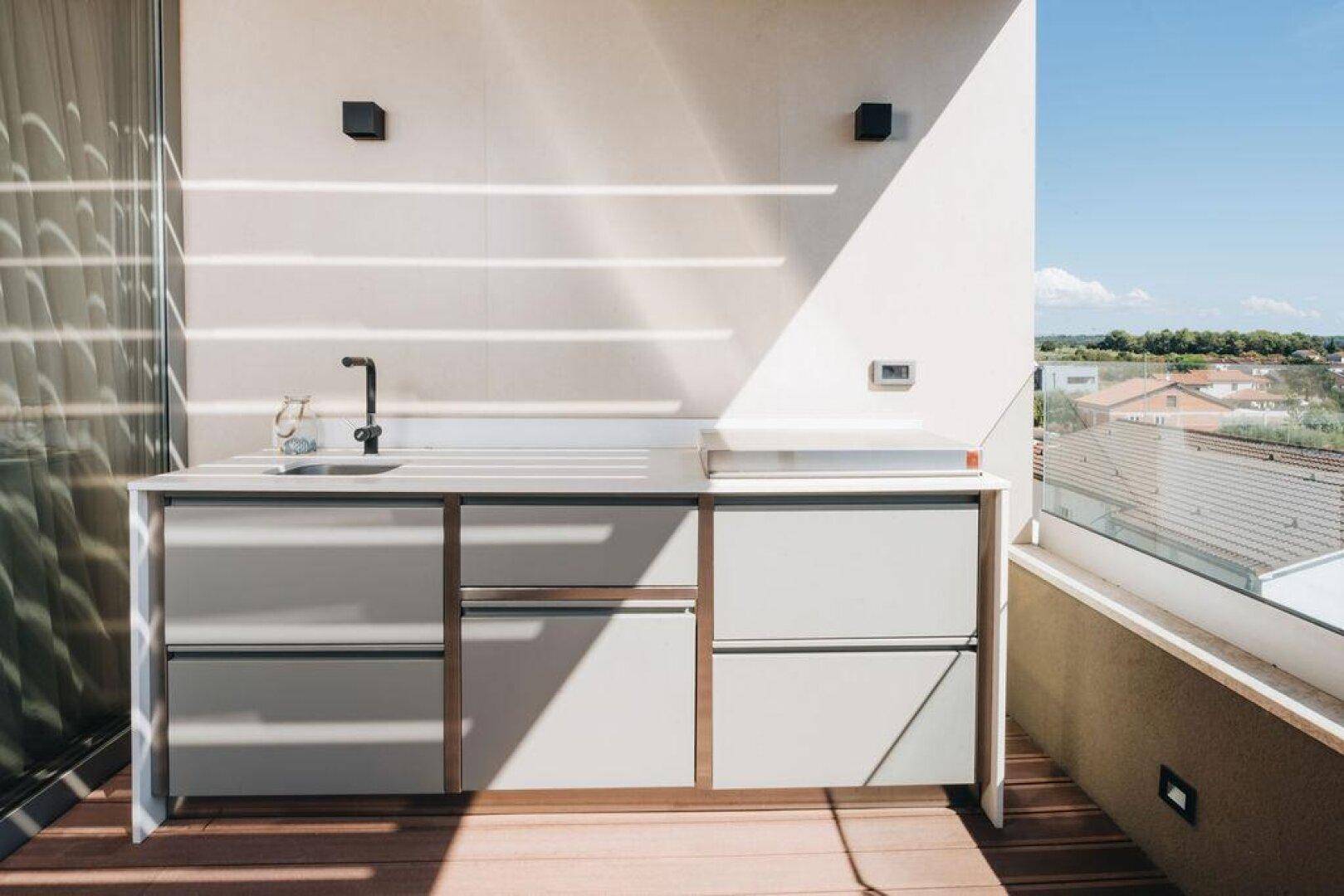 Sonniger Terrassenbereich mit Außenküche, Spüle und weitem Blick über die Landschaft.