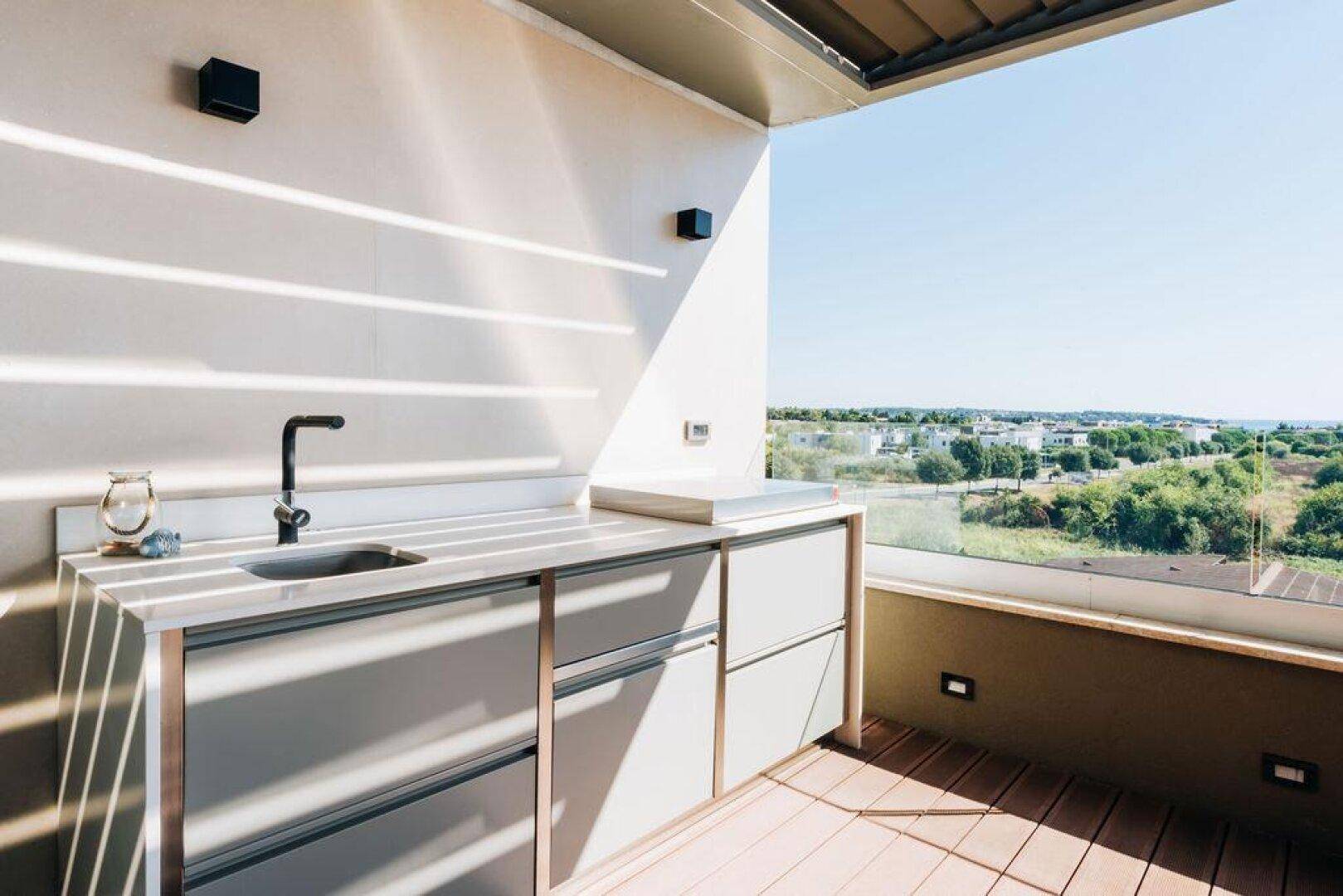 Außenküche auf einer sonnigen Terrasse mit Spüle und Panoramablick auf die Umgebung.