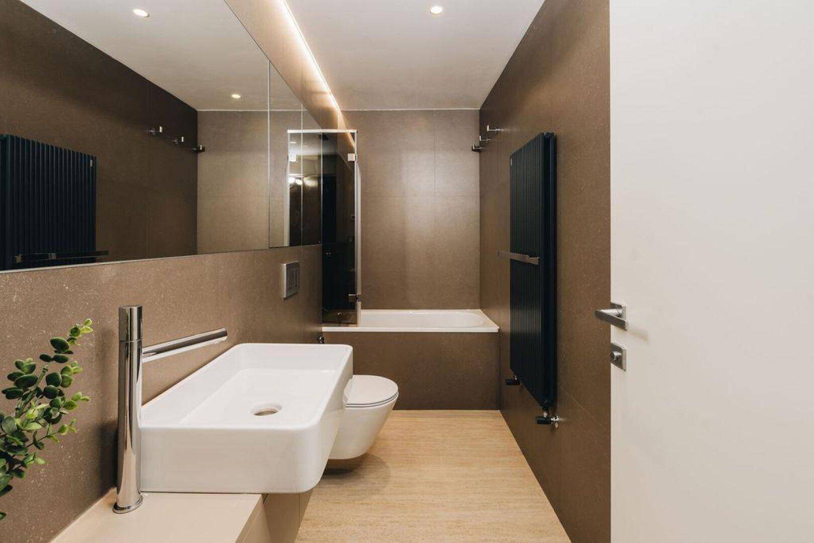 Modernes Badezimmer mit großem Spiegel, Waschtisch, Toilette und Badewanne in Brauntönen.