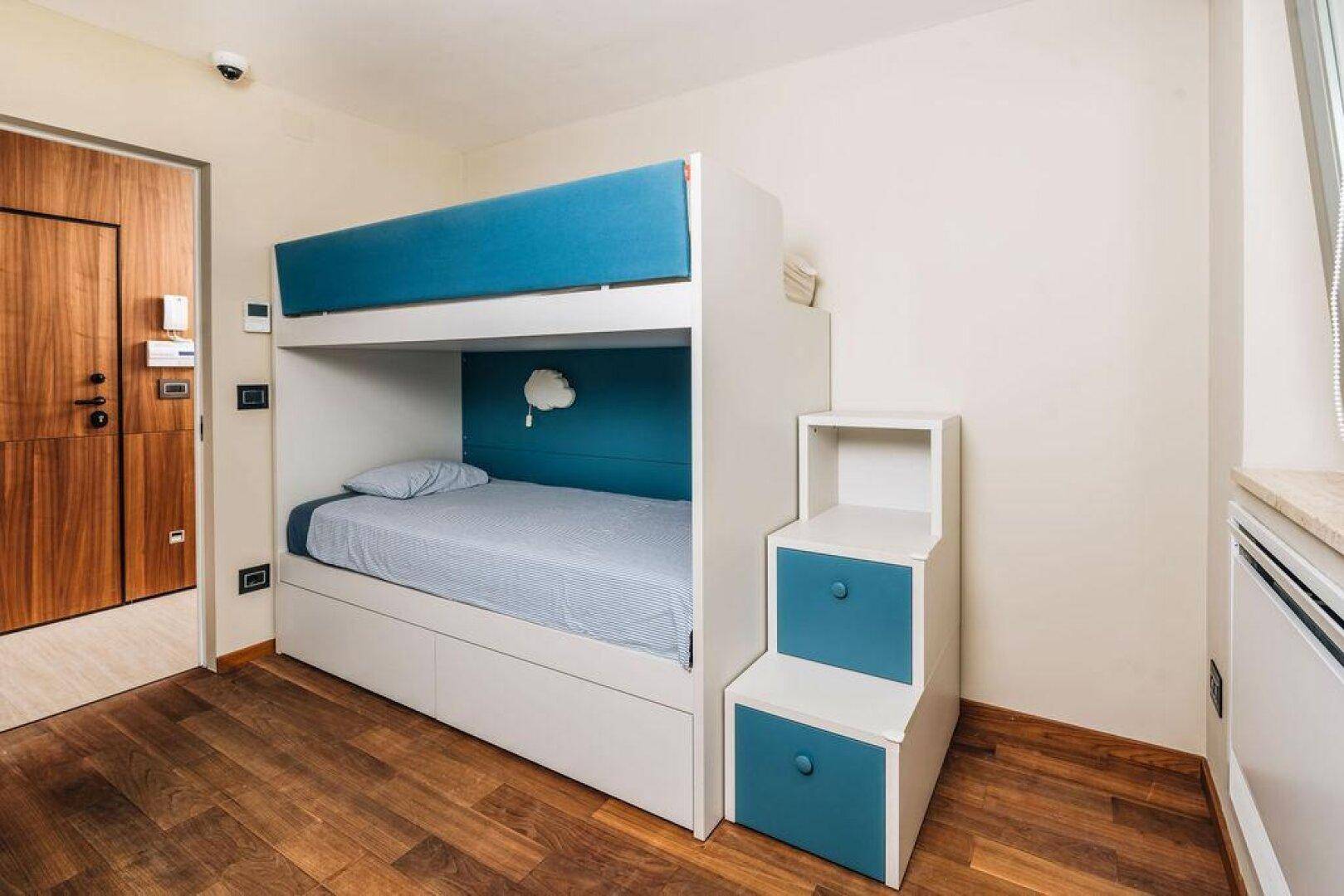 Kinderzimmer mit modernem Etagenbett in Weiß und Blau, Holzboden und Holztür.