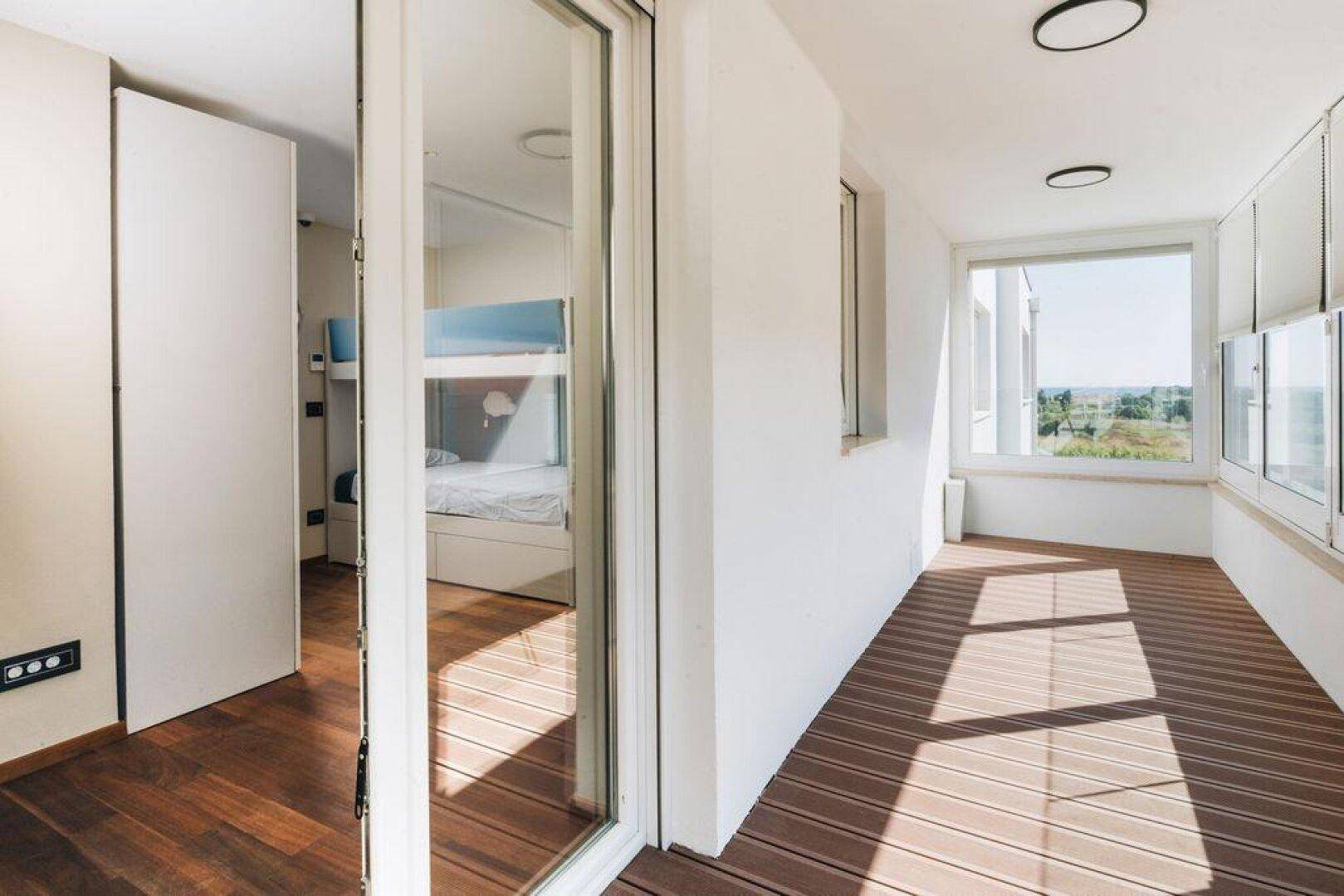 Heller Übergangsbereich mit Holzboden und Blick in ein Kinderzimmer sowie auf eine verglaste Loggia.