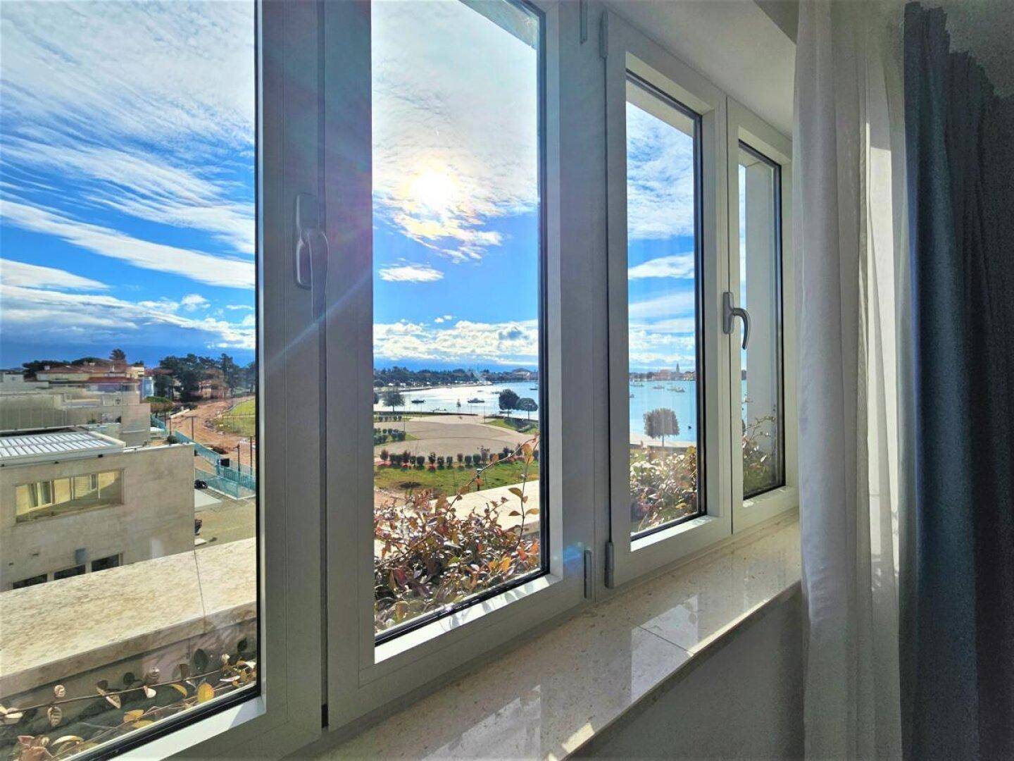 Heller Ausblick aus dem Fenster auf die sonnige Bucht mit Booten und grünen Ufern.