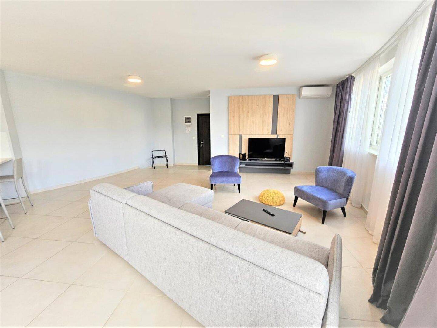 Geräumiges Wohnzimmer mit bequemem grauen Sofa, blauen Sesseln und einem modernen TV-Möbel.
