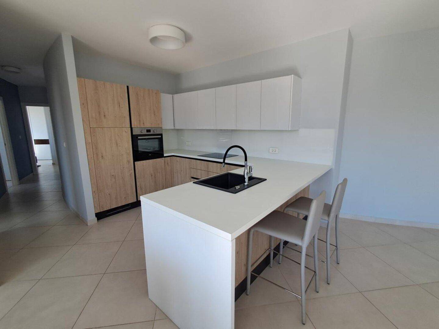 Moderne Küche mit Frühstücksbar und zwei Hockern, ausgestattet mit hellen Holz- und weißen Schränken.