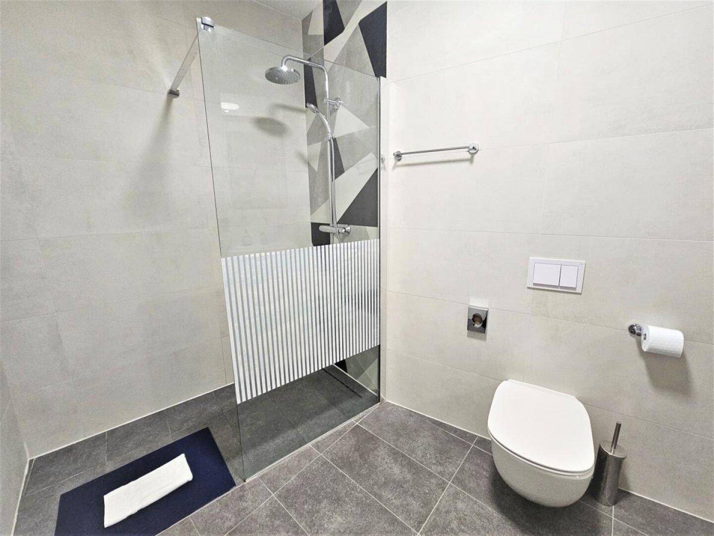 Modernes Badezimmer mit begehbarer Dusche, wandhängendem WC und stilvollen Fliesen.