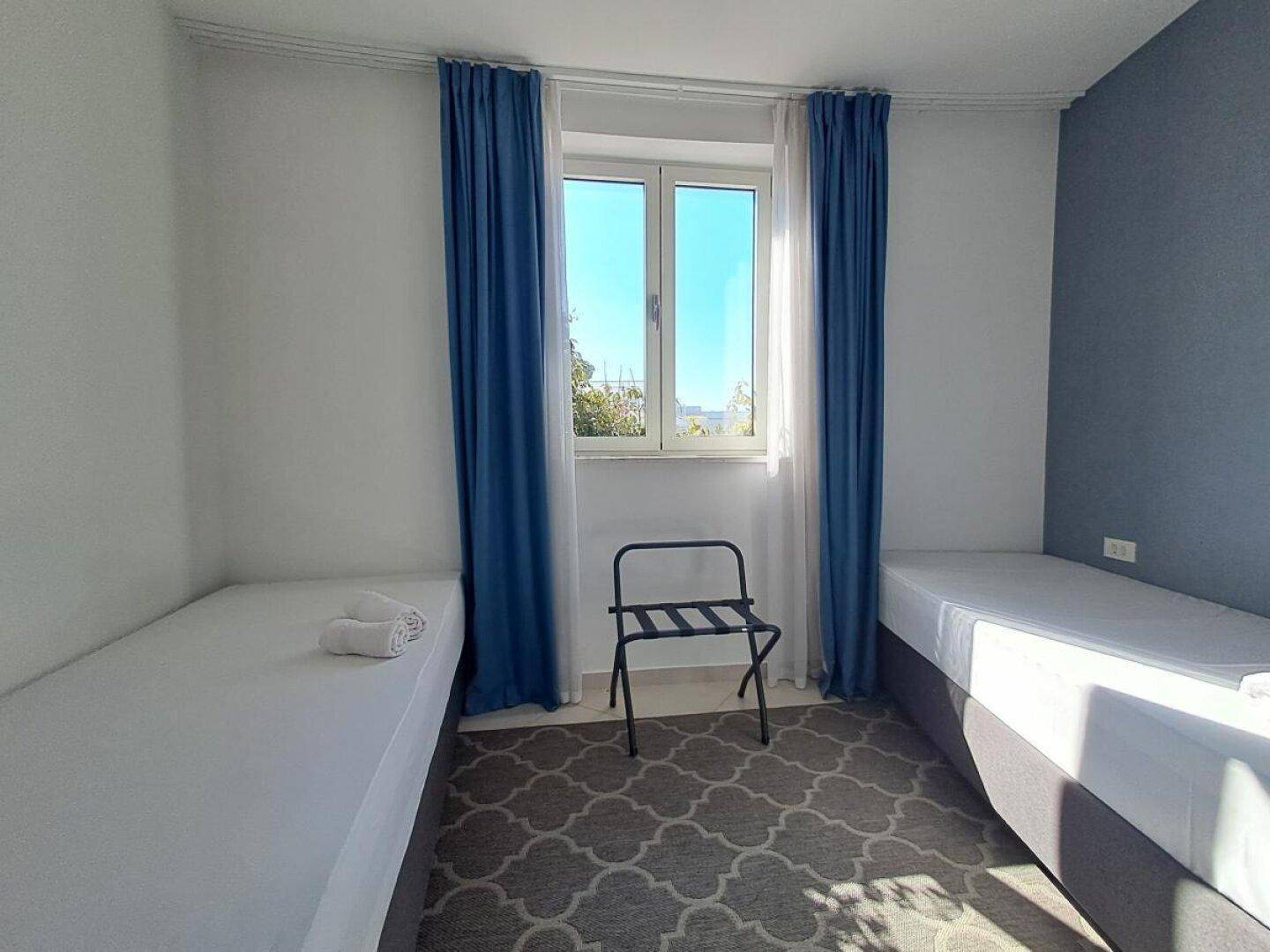 Helles Schlafzimmer mit zwei Einzelbetten, blauen Vorhängen und einem Fenster.