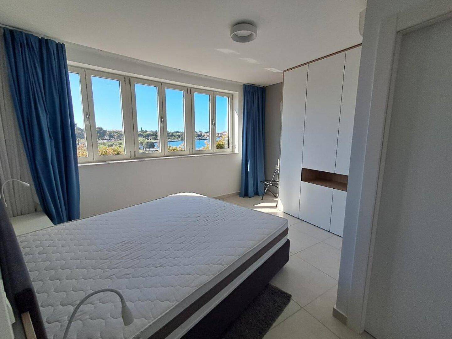 Geräumiges Schlafzimmer mit Doppelbett, blauen Vorhängen und einer Fensterfront mit Ausblick.