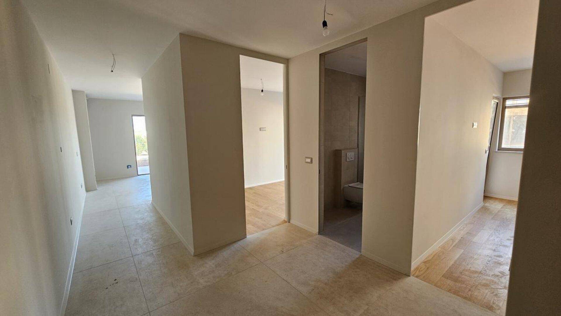 Heller Flur mit Fliesenboden und Zugang zu verschiedenen Räumen, teilweise im Rohbau.