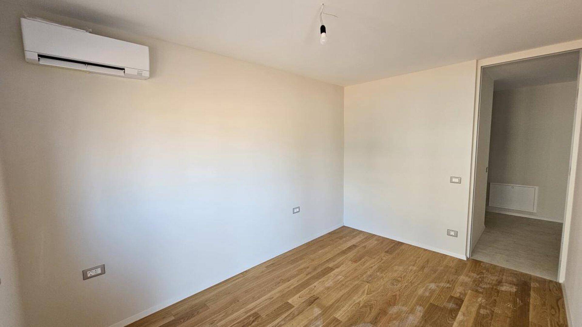Leeres Zimmer mit Holzboden und Klimaanlage, bereit für die individuelle Gestaltung.