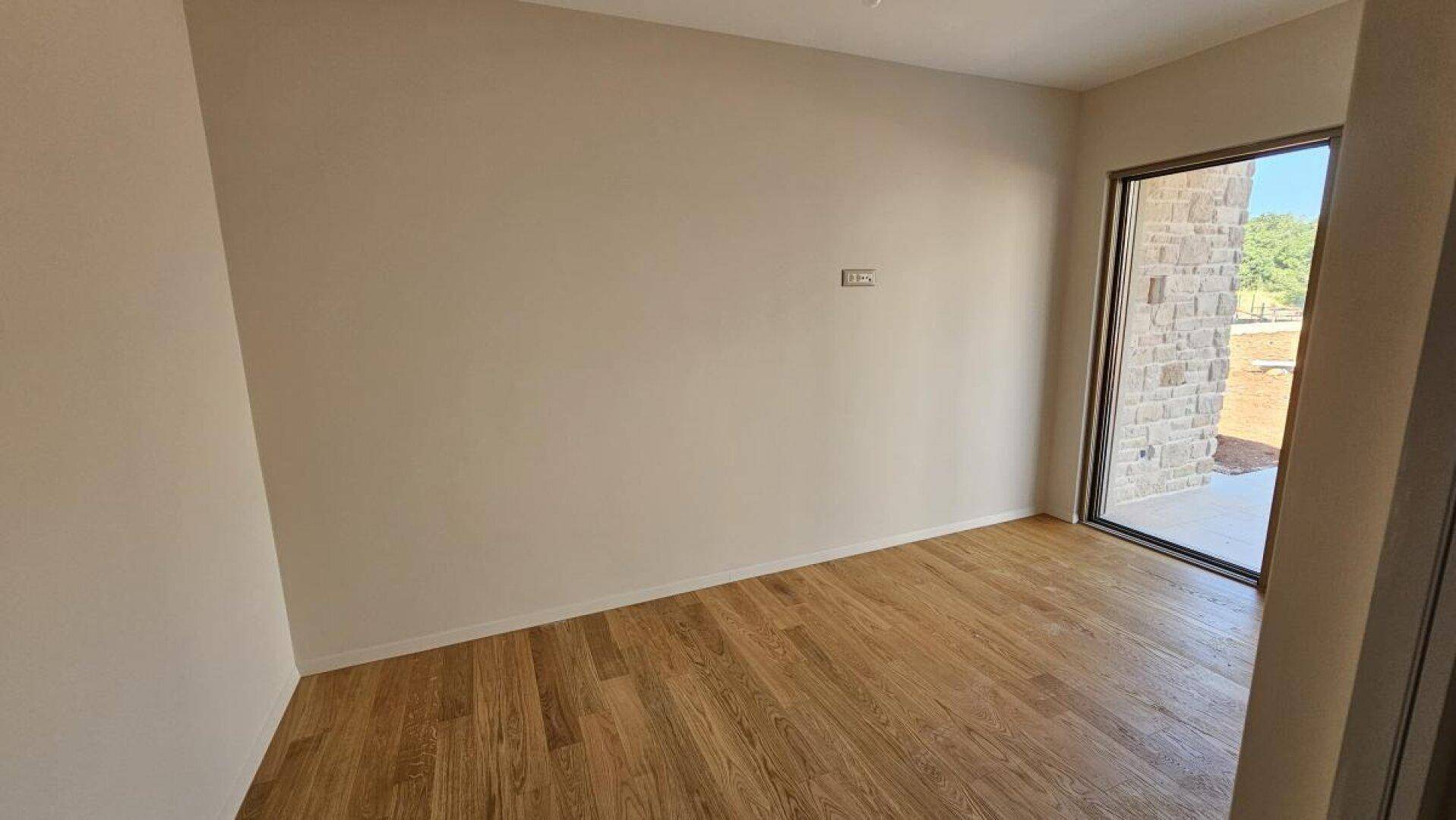 Helles Zimmer mit Holzboden und großer Fensterfront, die viel Tageslicht hereinlässt.