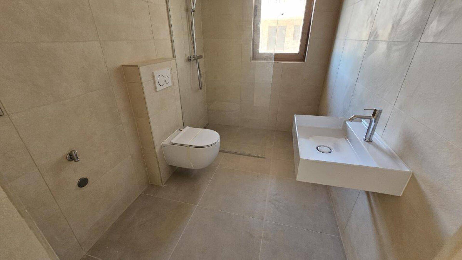 Modernes Badezimmer mit beigen Fliesen, wandhängendem WC und Duschbereich.