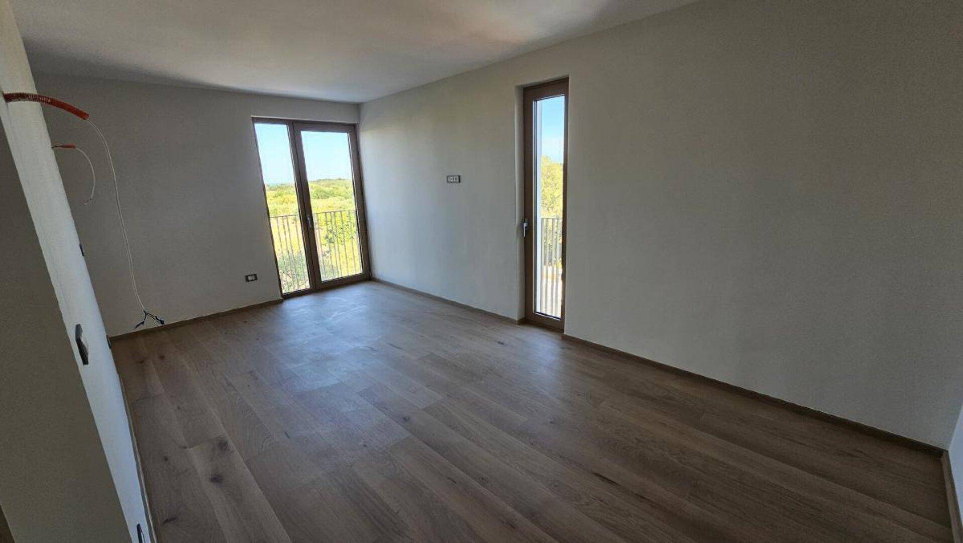 Helles Schlafzimmer mit Holzboden und zwei Fenstertüren, die viel Tageslicht hereinlassen.