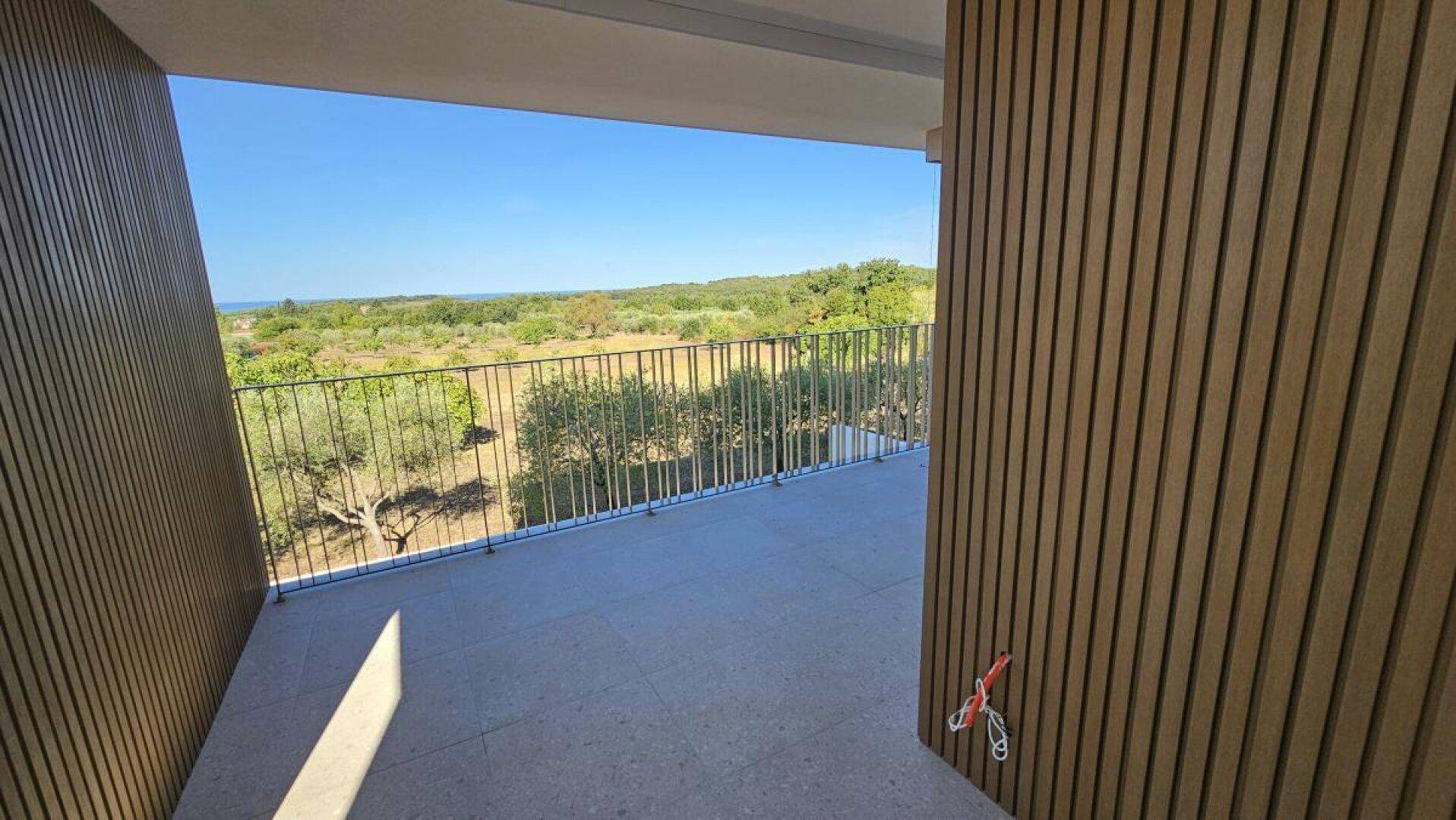 Balkon mit Holzverkleidung und weitem Blick auf die grüne Landschaft und das Meer.