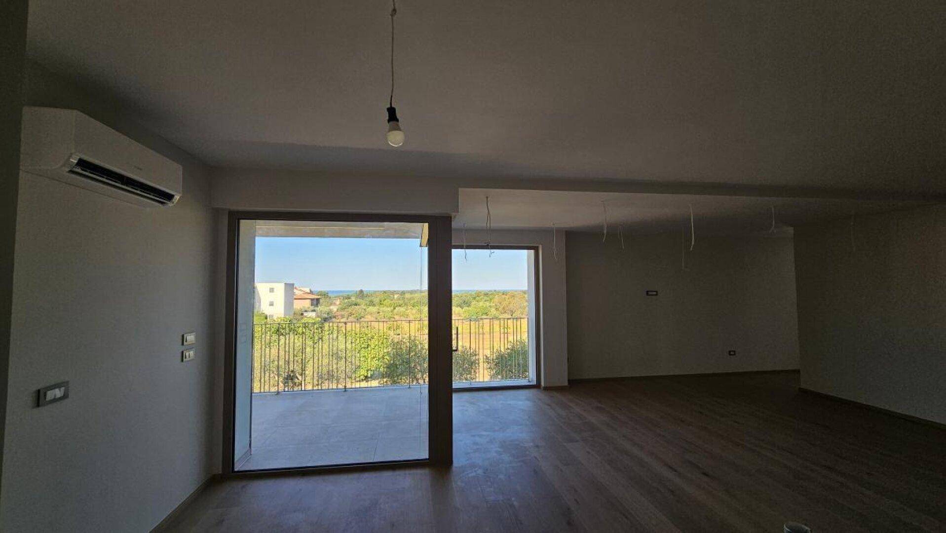 Heller Wohnbereich mit Holzboden, großen Fenstern und Zugang zum Balkon mit Meerblick.