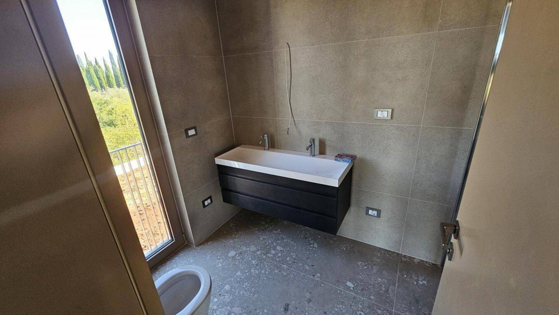 Modernes Badezimmer im Bau mit schwebendem Waschtisch, WC und großem Fenster.