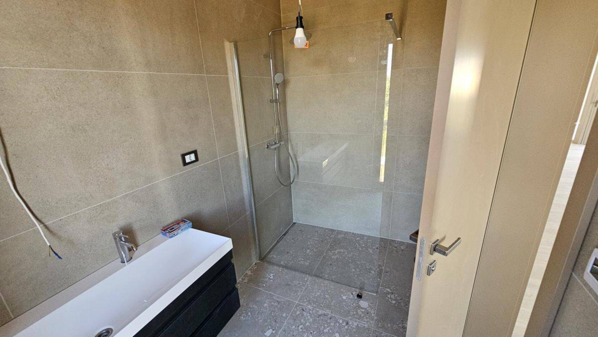 Badezimmer mit moderner begehbarer Dusche, schwebendem Waschtisch und Fliesenboden.