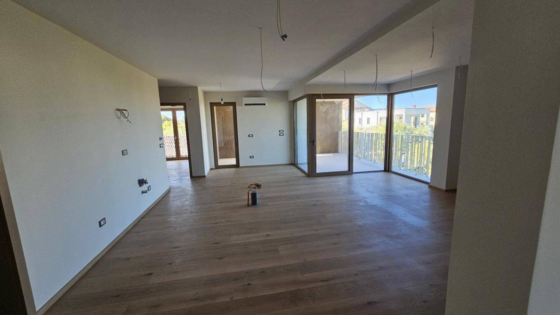 Großer, heller Wohn-Essbereich mit Holzboden und mehreren Zugängen zum Balkon.