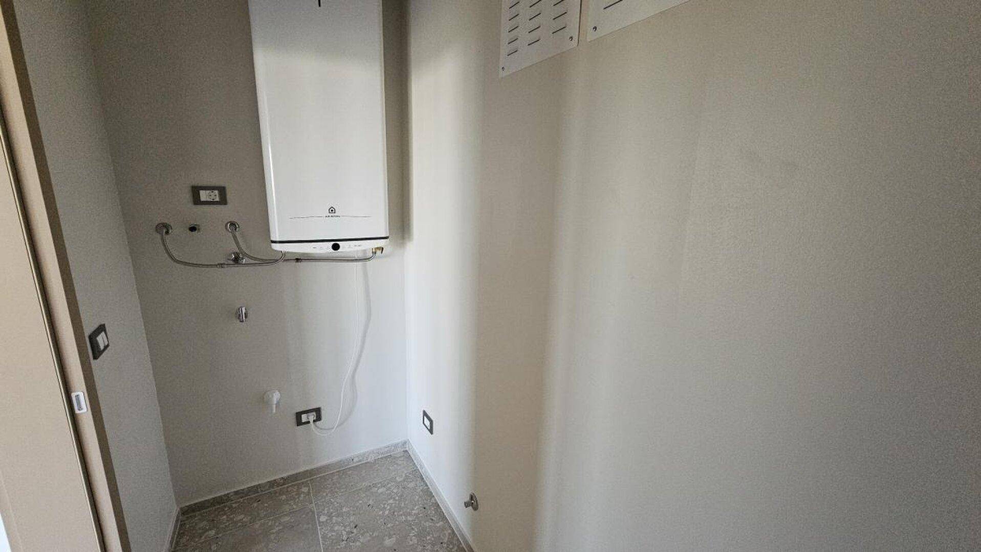 Praktischer Hauswirtschaftsraum mit Wandboiler und Fliesenboden für technische Installationen.