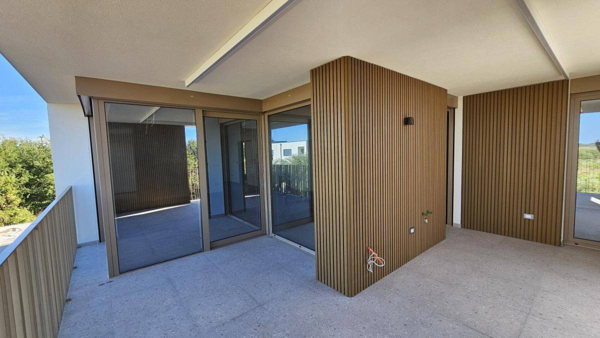 Geräumiger Balkon mit Fliesenboden und Holzverkleidung, direktem Zugang zum Innenbereich.