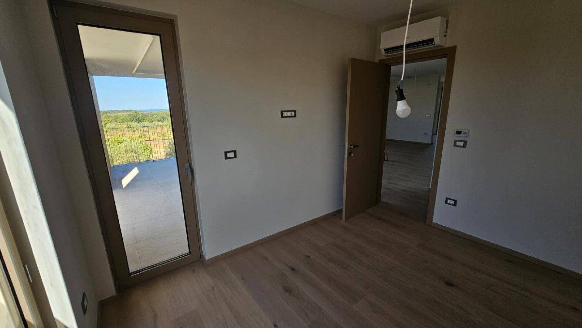 Schlafzimmer mit Holzboden, Klimaanlage und Zugang zu einem sonnigen Balkon.