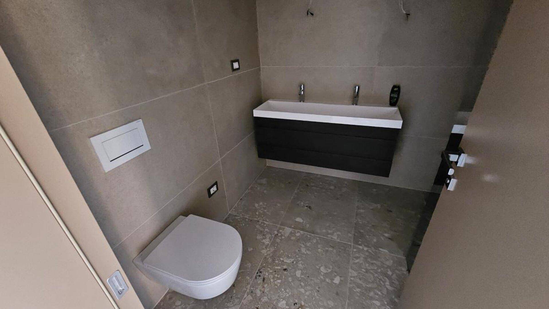 Modernes Badezimmer mit Doppelwaschtisch, wandhängender Toilette und Fliesenboden.