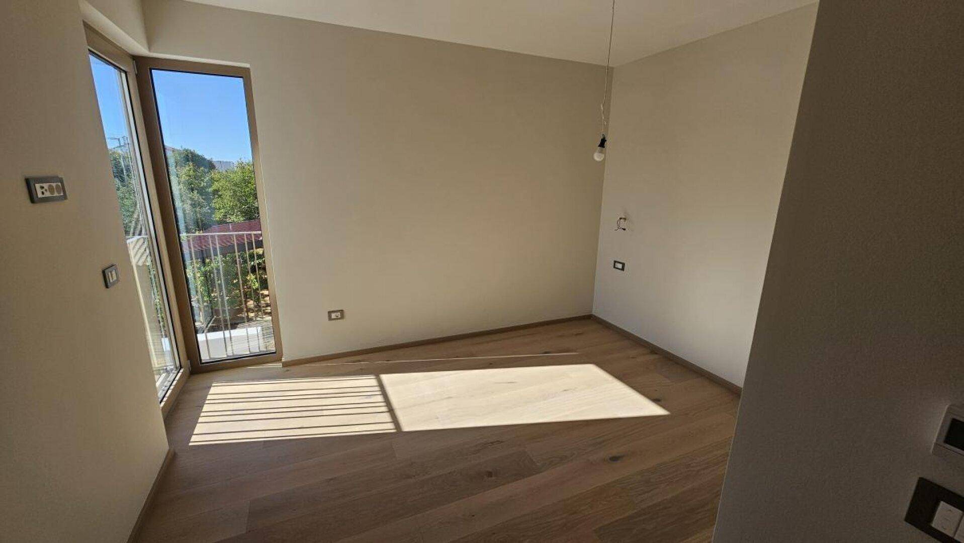 Helles Schlafzimmer mit Holzboden und viel natürlichem Licht durch die große Fenstertür.