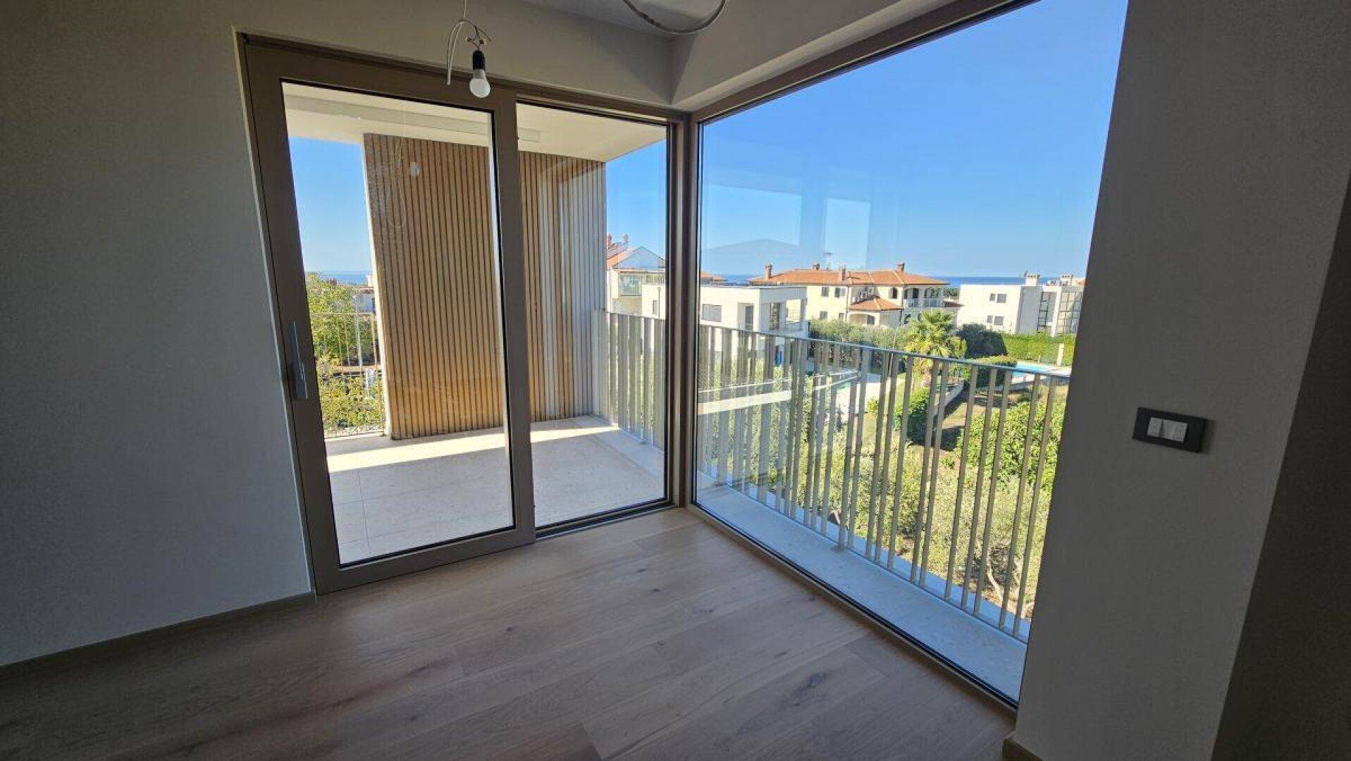 Heller Innenraum mit großen Fenstern, Schiebetür zum Balkon und Blick auf die Umgebung und das Meer.