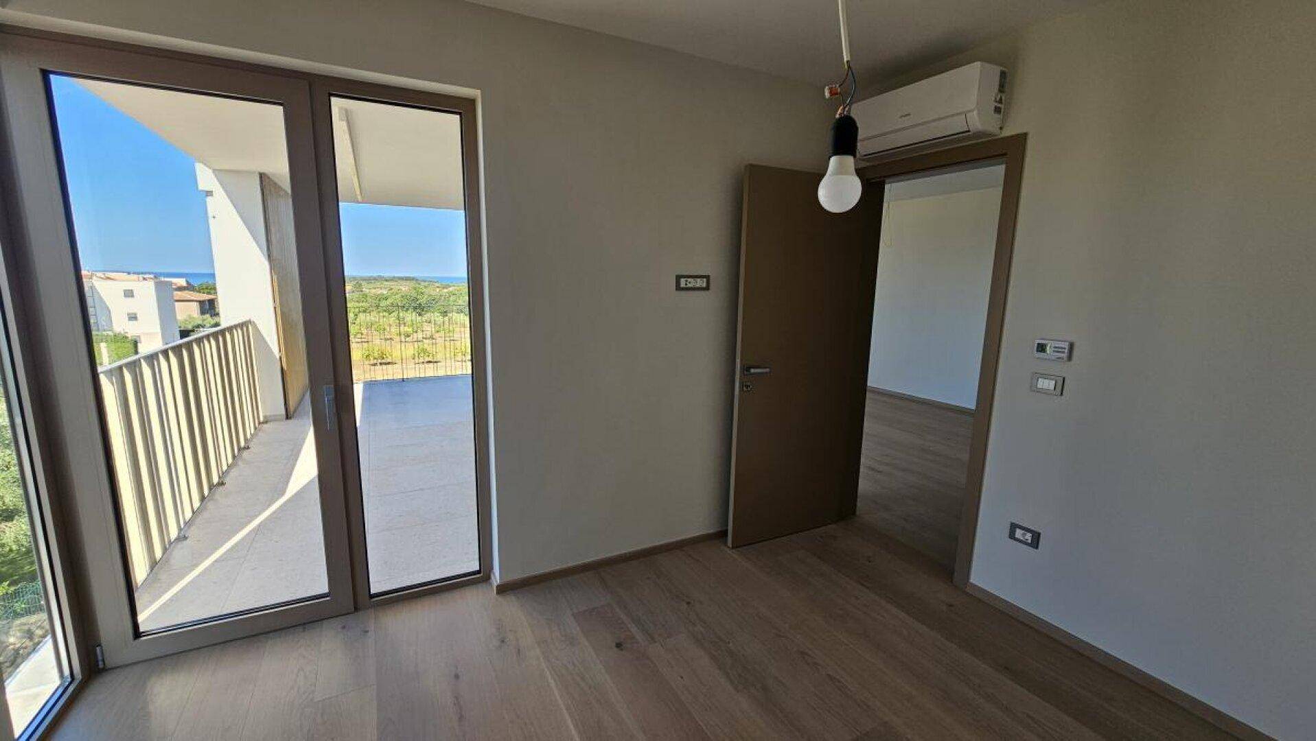 Schlafzimmer mit Holzboden, Balkonzugang und Klimaanlage, bereit für die persönliche Einrichtung.