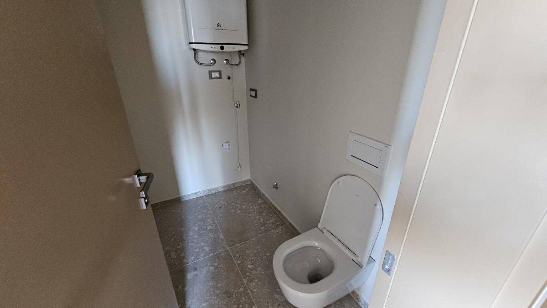 Kleiner WC-Raum mit Toilette und Warmwasserbereiter, funktional und praktisch gestaltet.