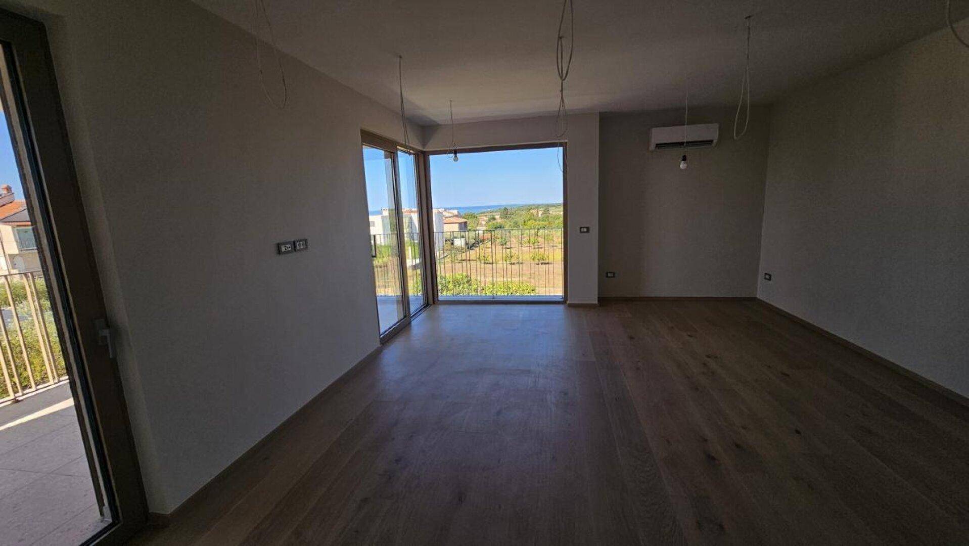Geräumiges Wohnzimmer mit Holzboden, Zugang zum Balkon und weitem Blick auf das Meer und die Landschaft.