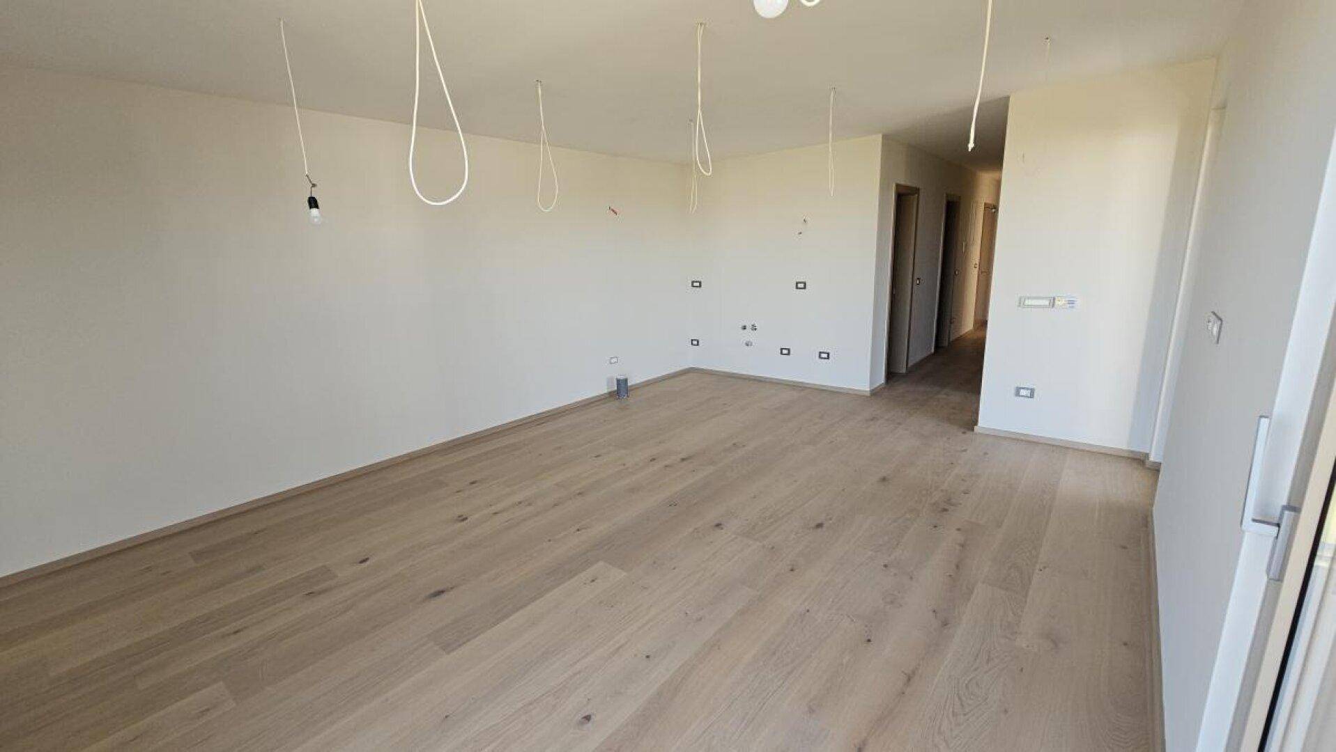 Heller, leerer Raum mit neuem Holzboden und Zugang zu weiteren Zimmern, ideal für individuelle Gestaltung.