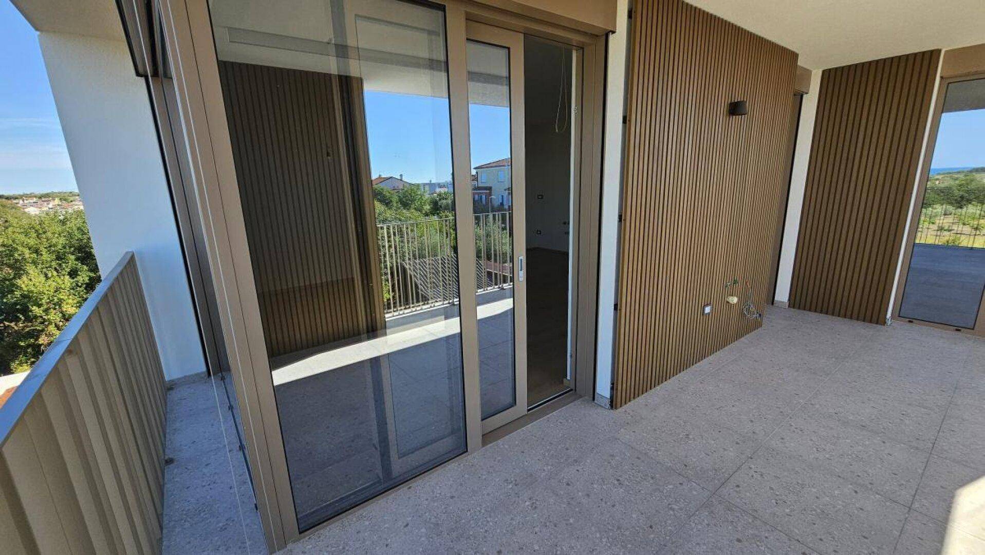 Moderner Balkon mit Holzverkleidung und Schiebetüren, bietet Zugang zu den Innenräumen und Grünblick.