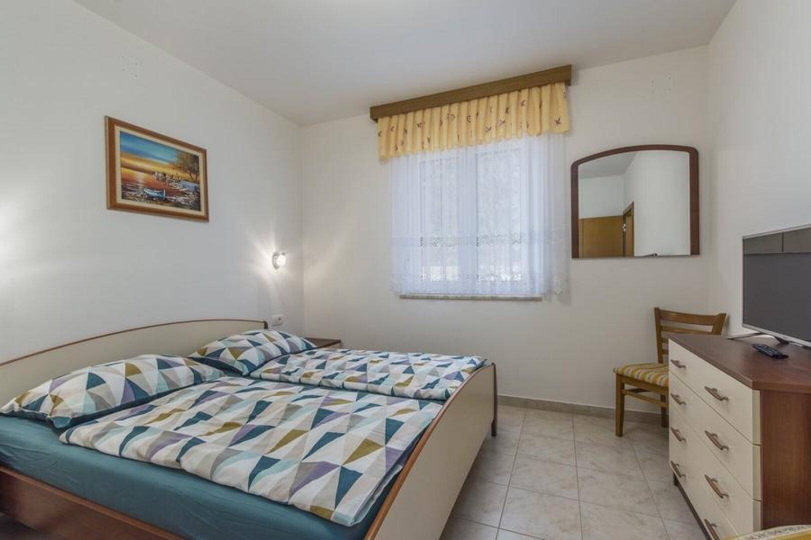 Gemütliches Schlafzimmer mit Doppelbett, Nachttisch und Fernseher, hell gefliest.
