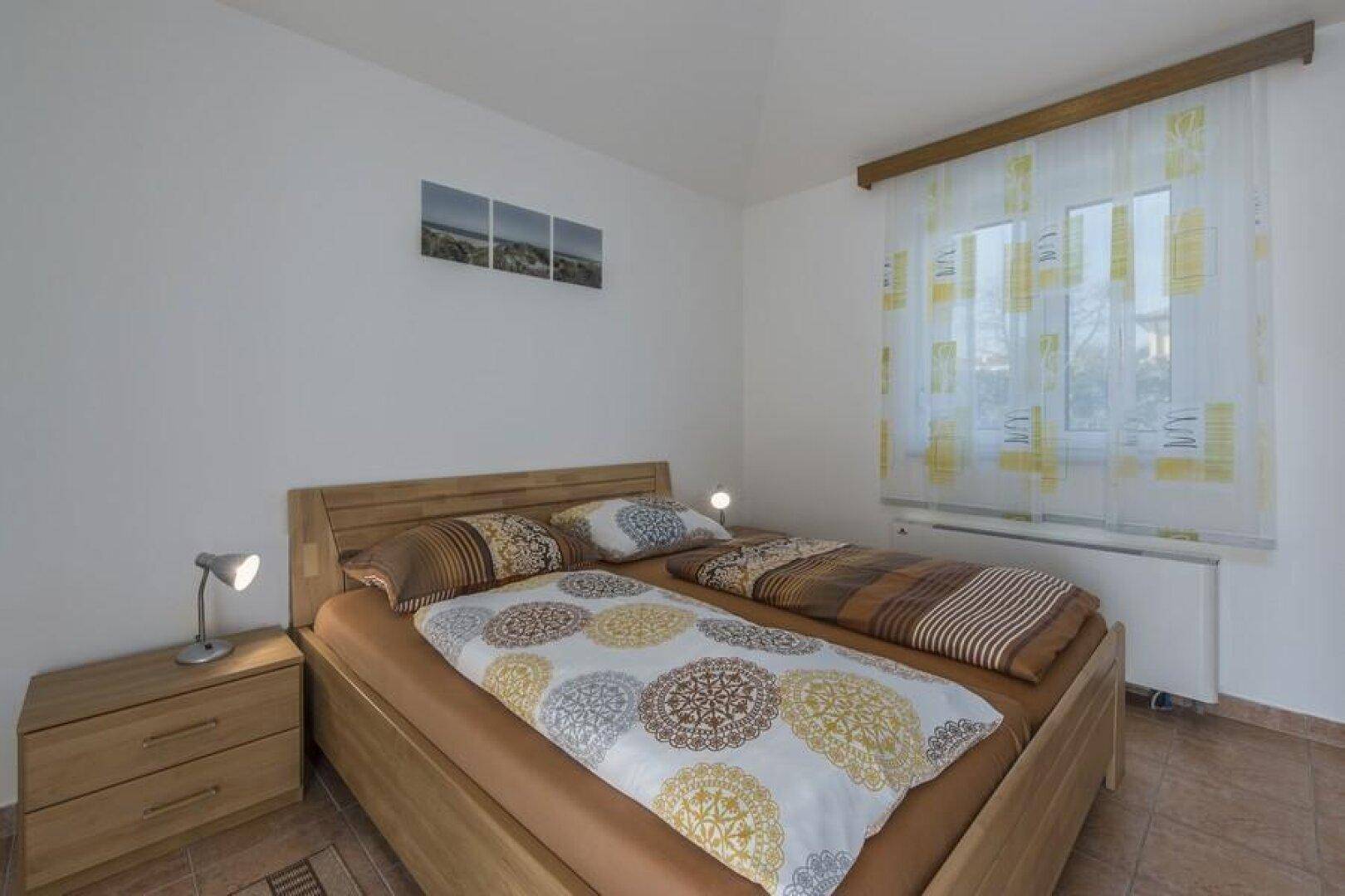 Komfortables Schlafzimmer mit Doppelbett, Nachttisch und Heizkörper unter dem Fenster.