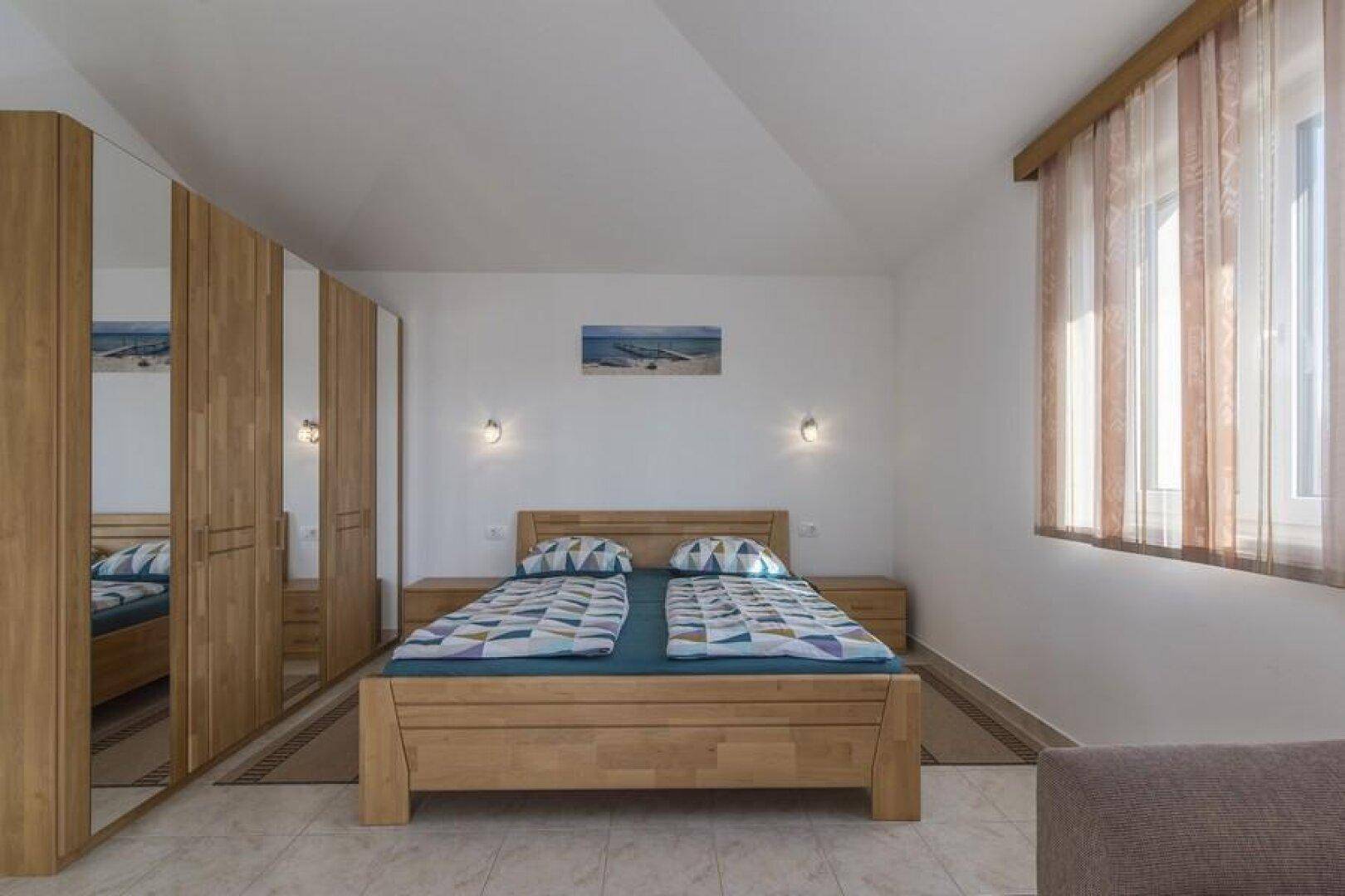 Geräumiges Schlafzimmer mit Holzdoppelbett, Nachttischen und großem Fenster für viel Licht.
