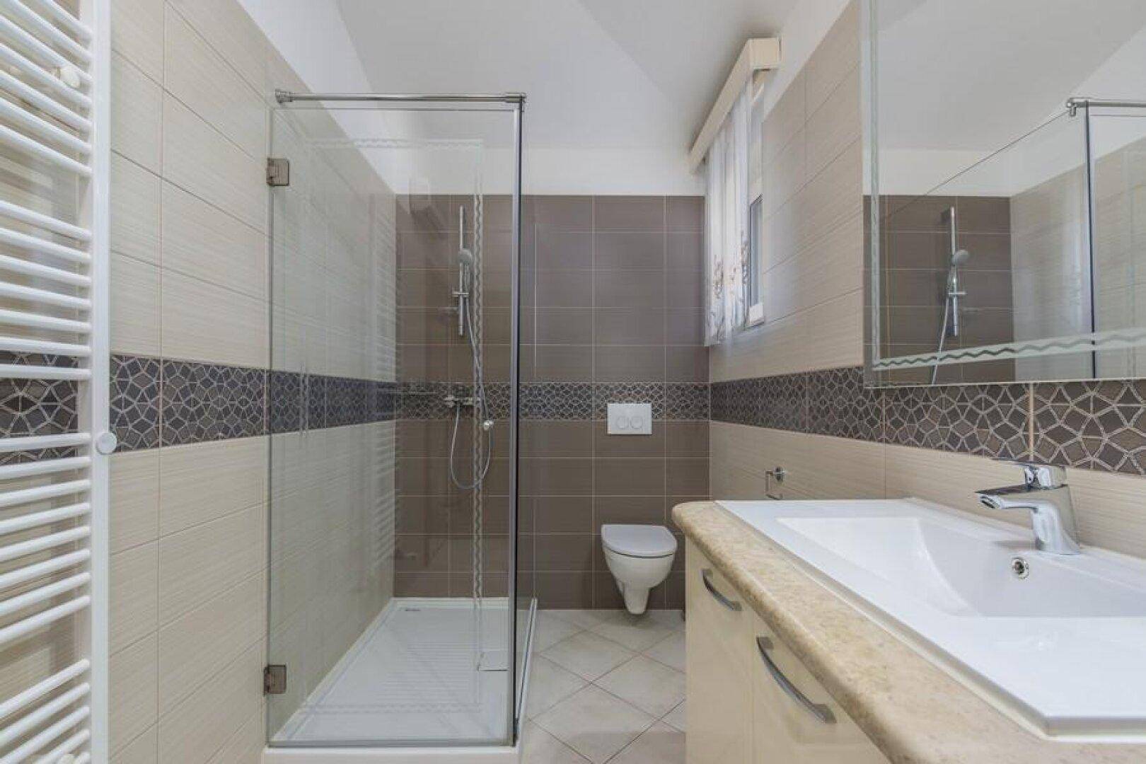 Helles Badezimmer mit ebenerdiger Dusche, Wand-WC und Waschbecken mit Spiegelschrank.