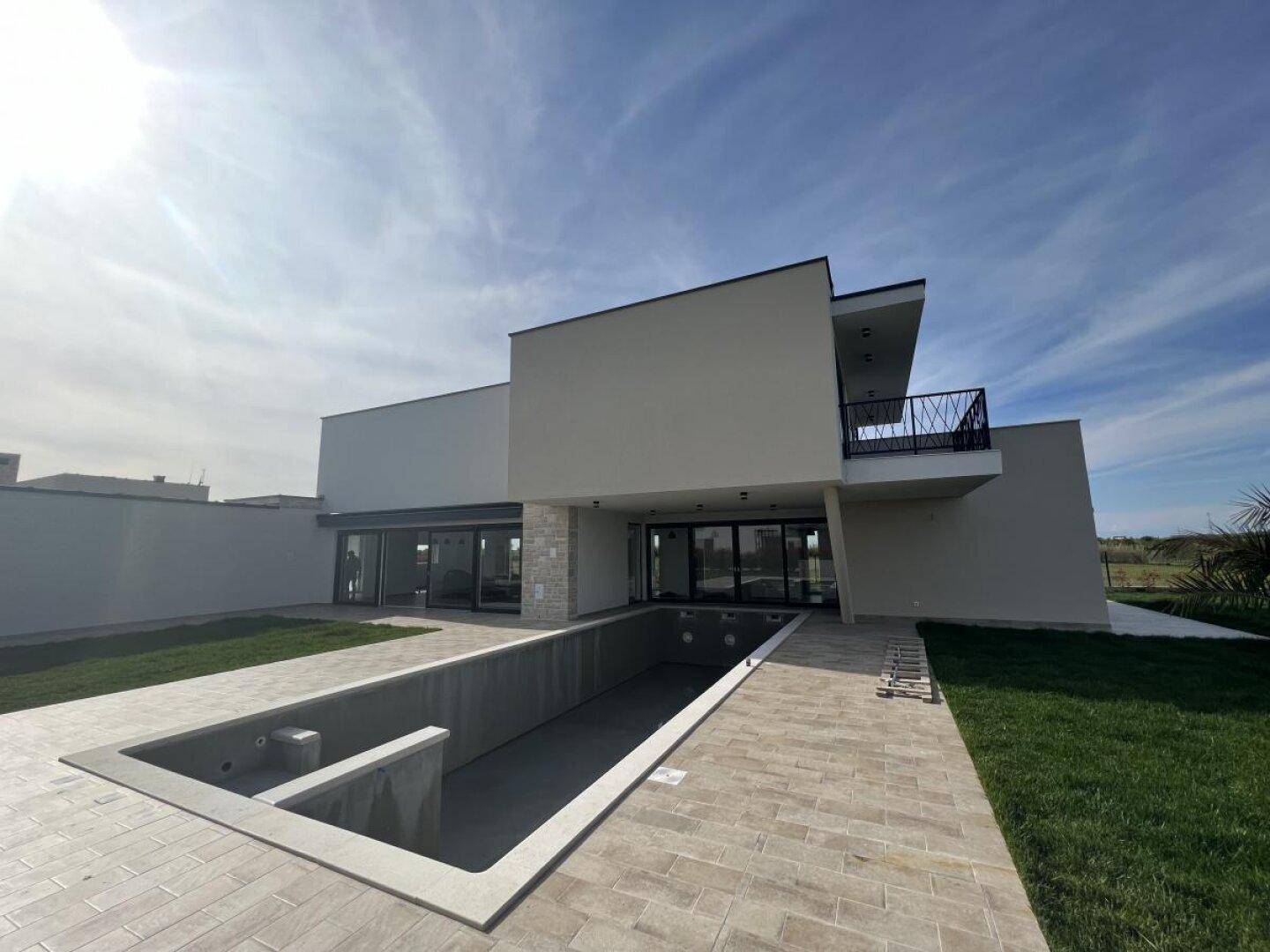 Rückansicht der modernen Villa mit einem noch unfertigen Swimmingpool und weitläufigem Garten.