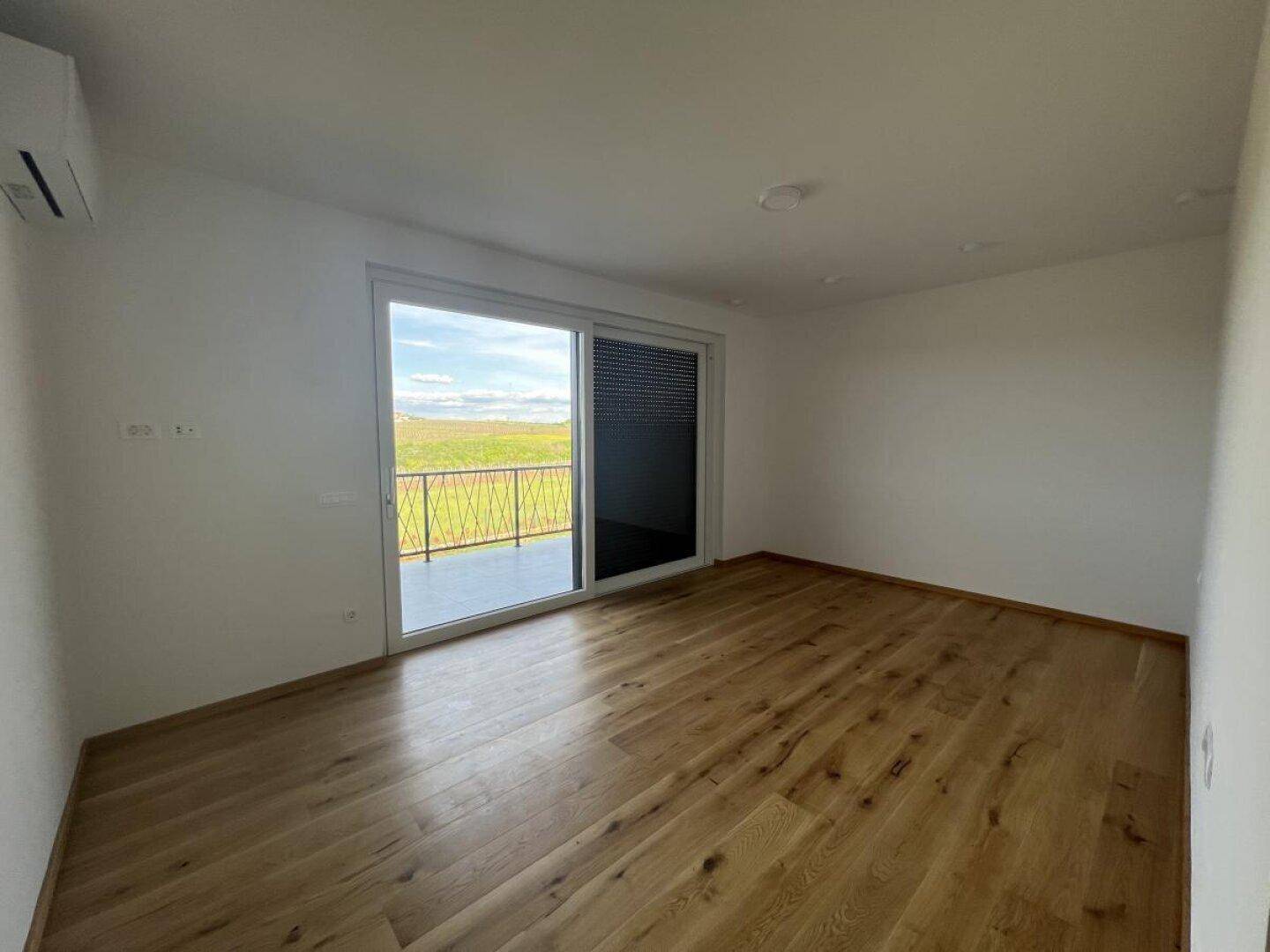 Helles Zimmer mit Holzboden, Klimaanlage und Zugang zu einem Balkon mit Weitblick.