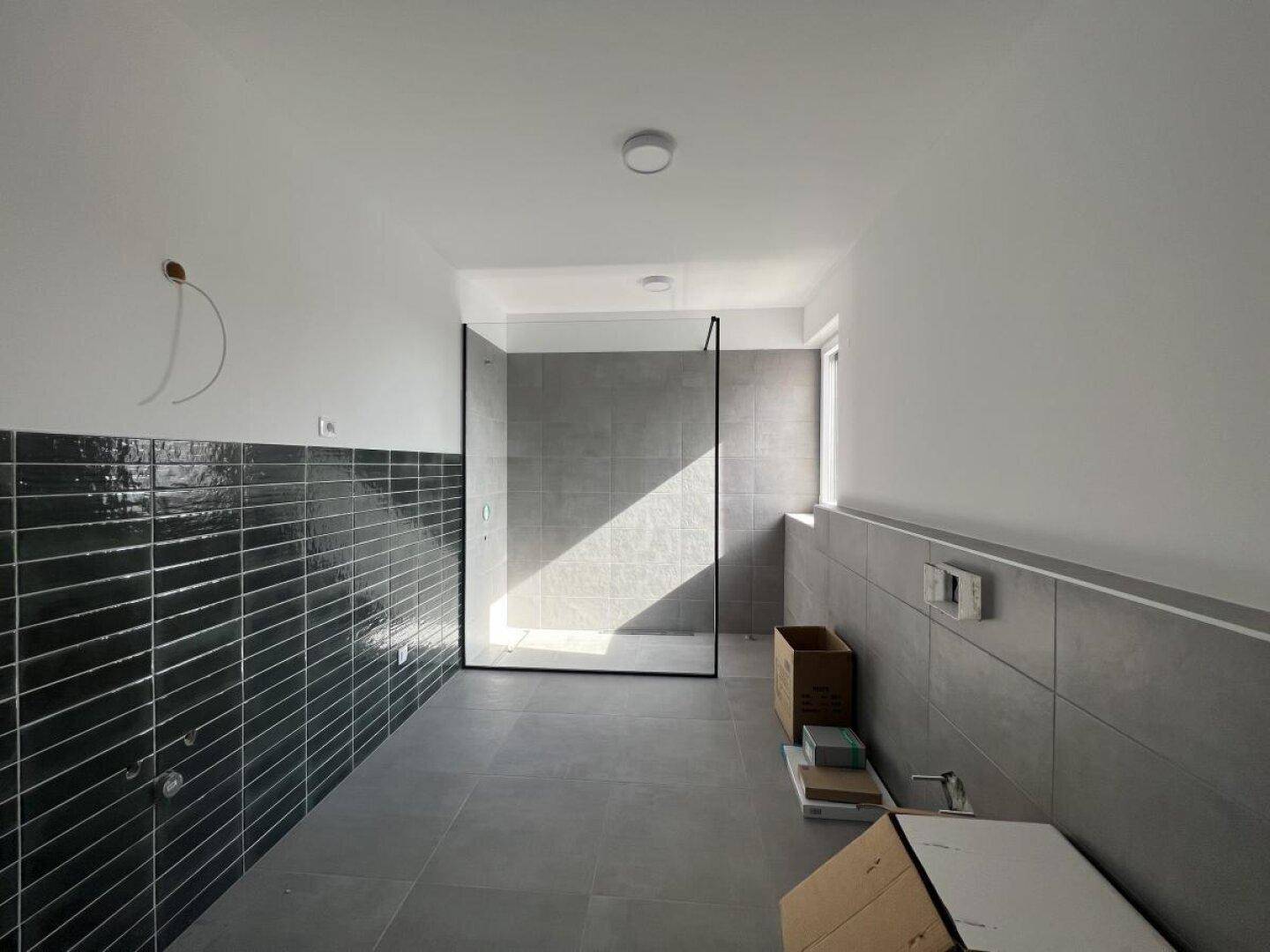 Modernes Badezimmer im Bau mit grauen Fliesen und einer begehbaren Duschkabine.