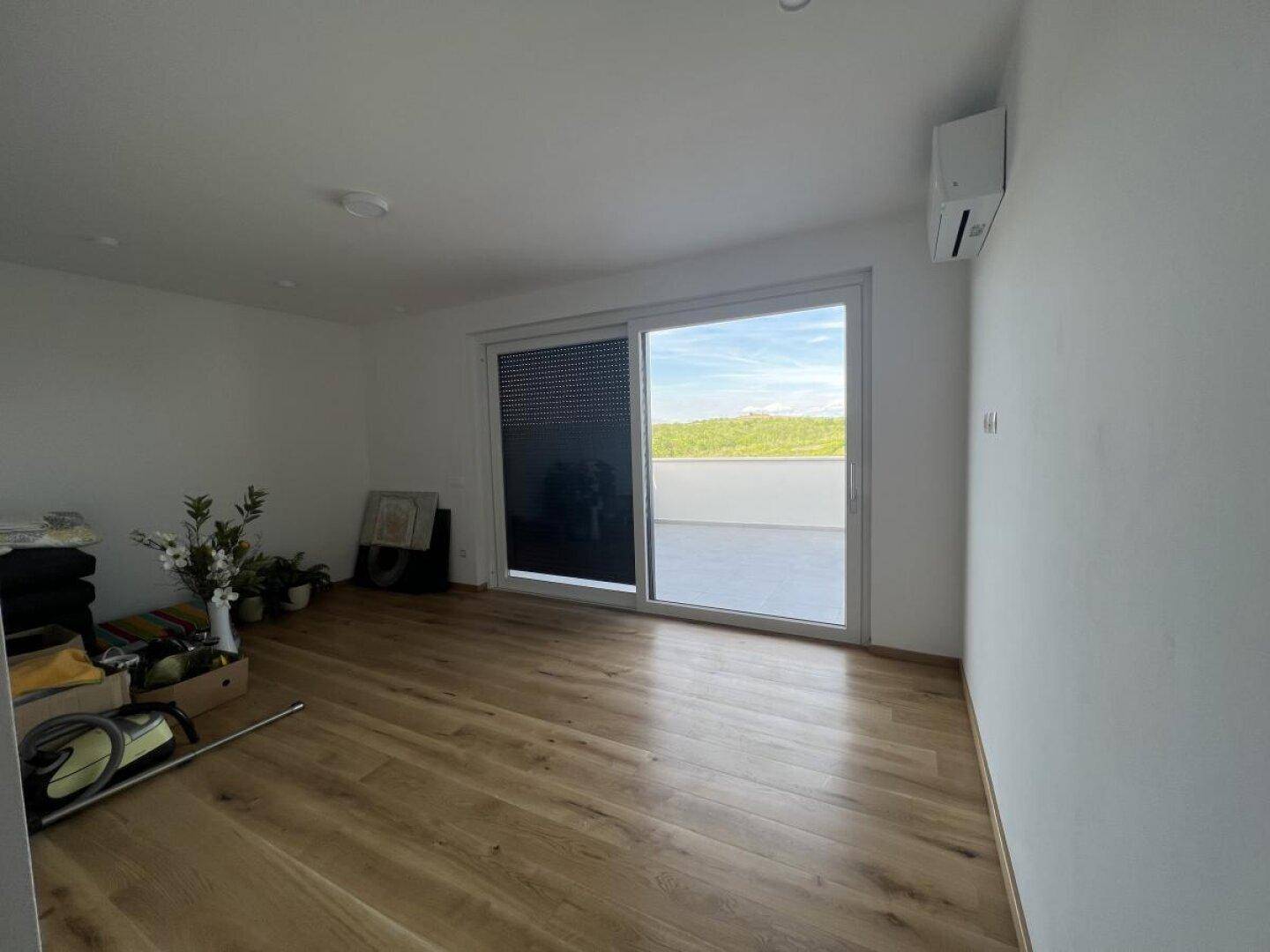 Helles Zimmer mit Holzboden und großem Schiebetürzugang zu einer Außenterrasse.