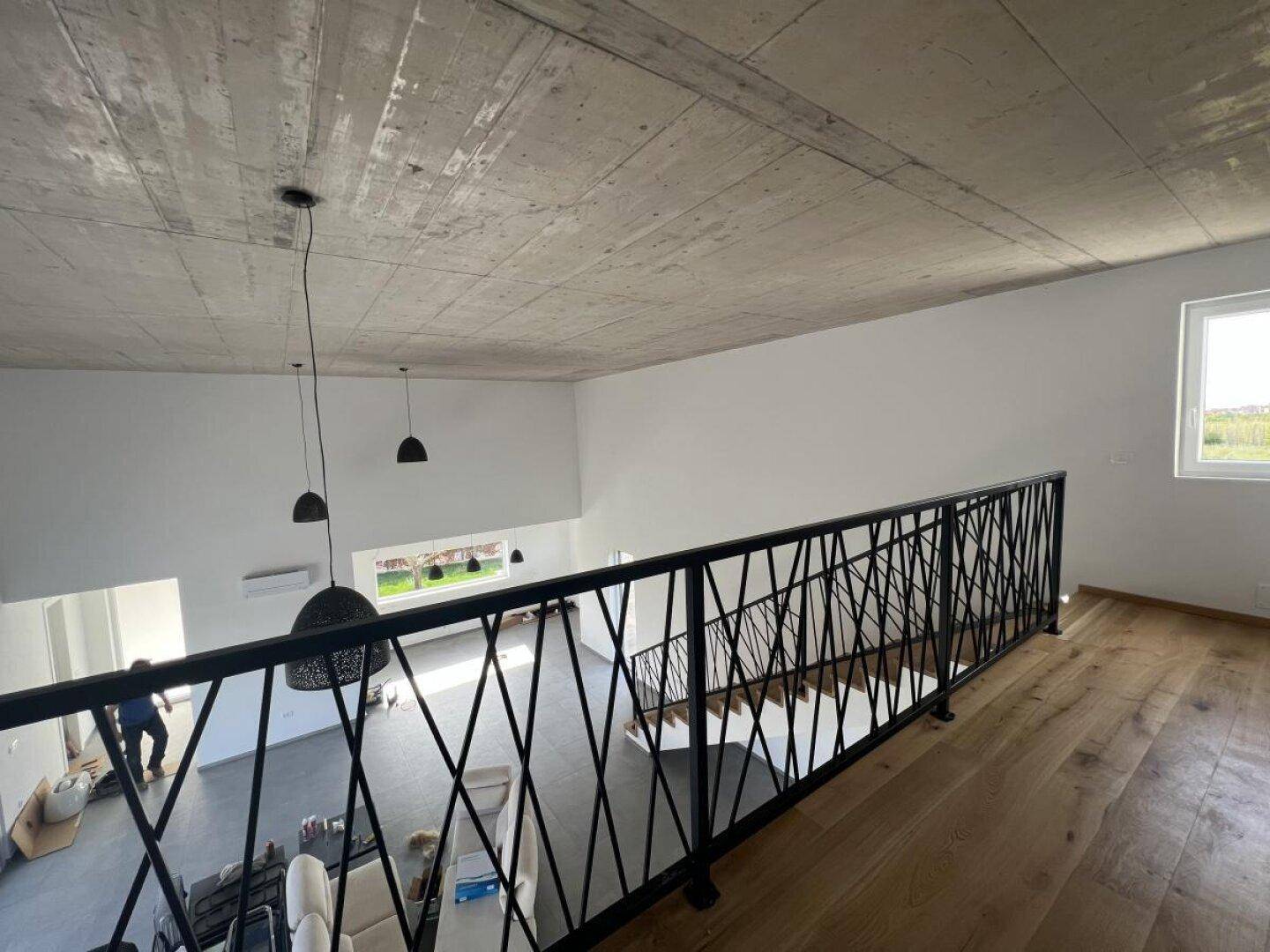 Offener Wohnbereich mit hoher Decke, Sichtbeton und moderner Galerie mit Geländer.