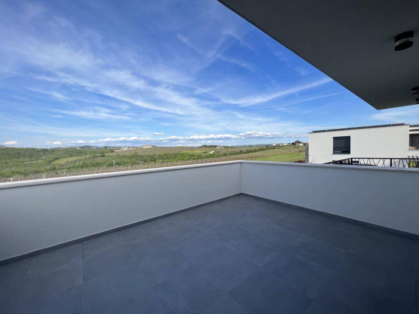Große Dachterrasse mit Fliesenboden und weitem Blick über die grüne Landschaft.